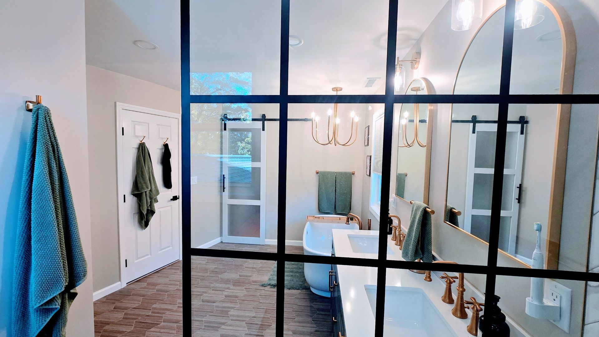 Bathroom remodeling in Wolcott, CT with glass-paneled partition, white vanity, and gold fixtures. Green towels and a hanging chandelier are visible.