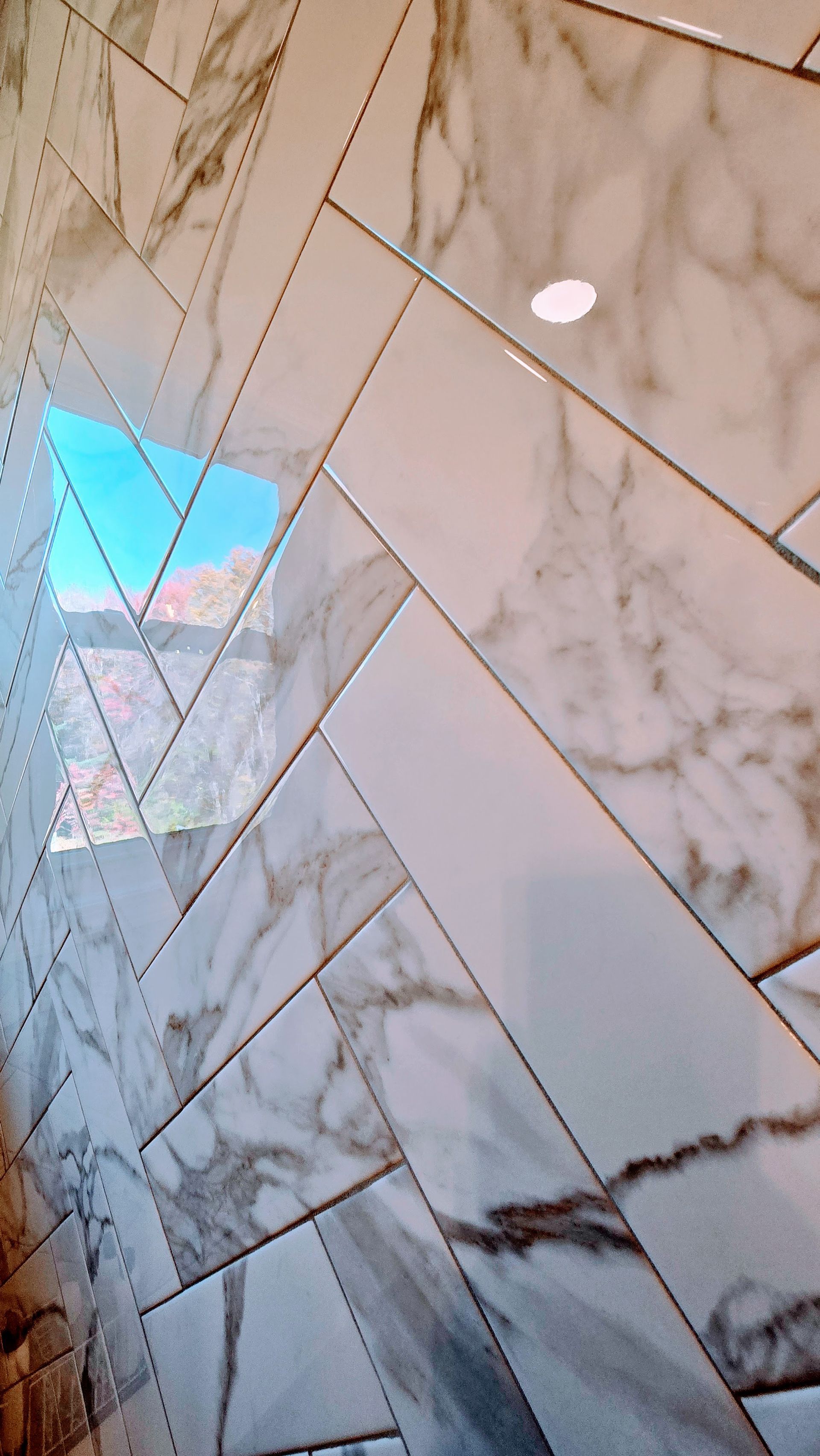 Herringbone tiled wall in the shower in Wolcott, CT with sky view. White marble tiles with gold trim.