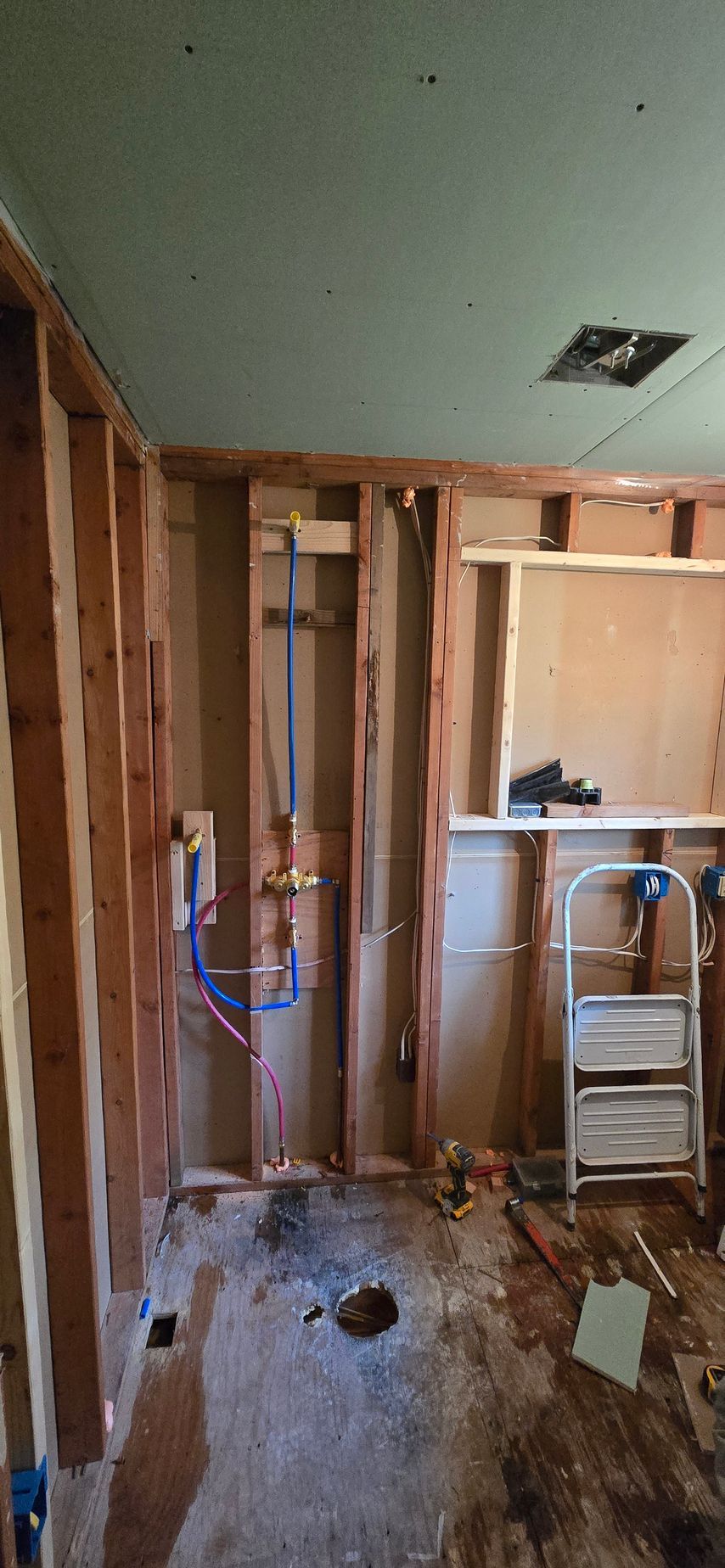 Bathroom in framing stage in Glastonbury, CT. Wooden studs, plumbing visible, ladder, damaged floor, and ceiling.
