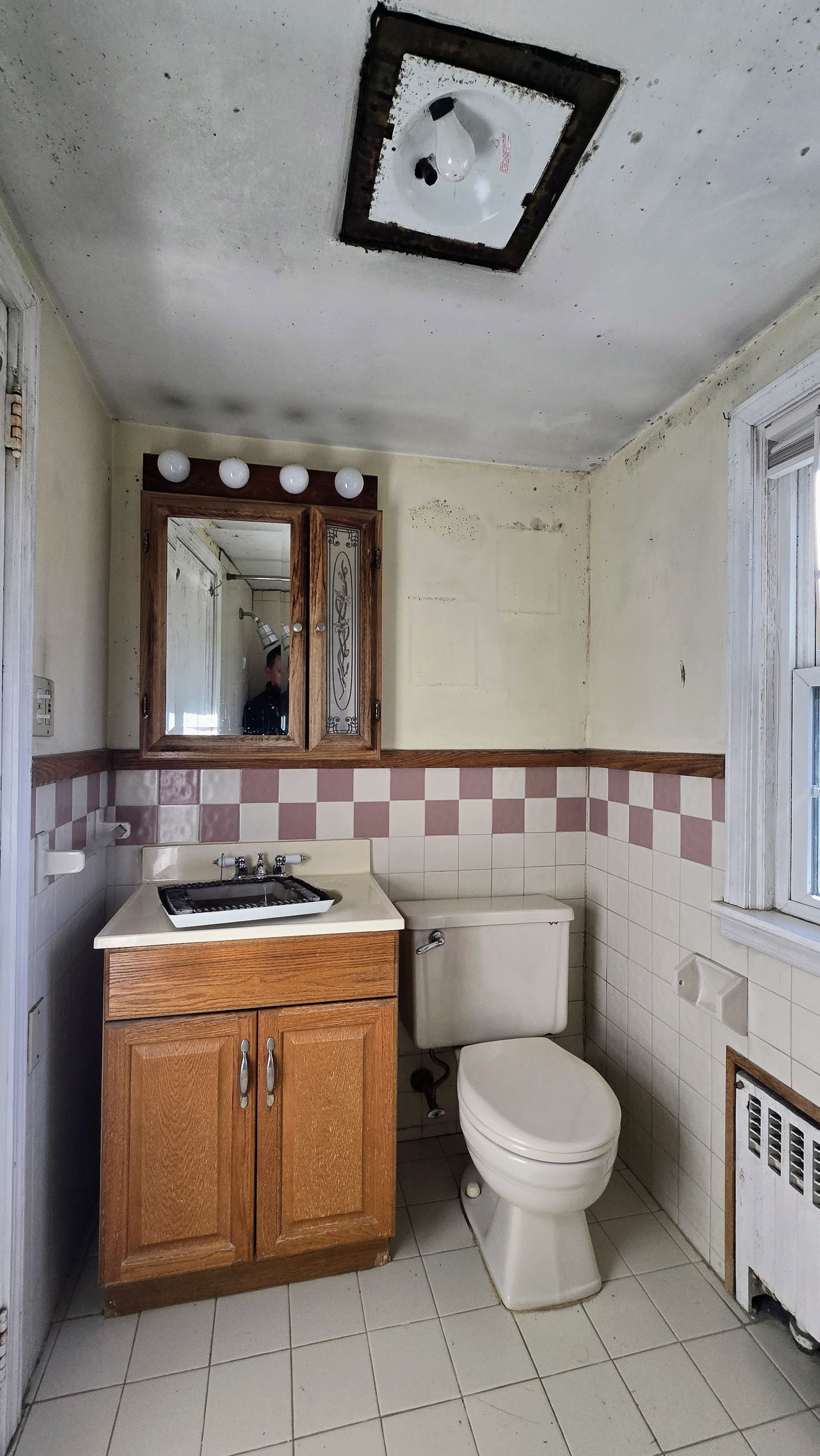Small Southington CT bathroom with brown vanity, toilet, and checkered tile trim. Ceiling light fixture.
