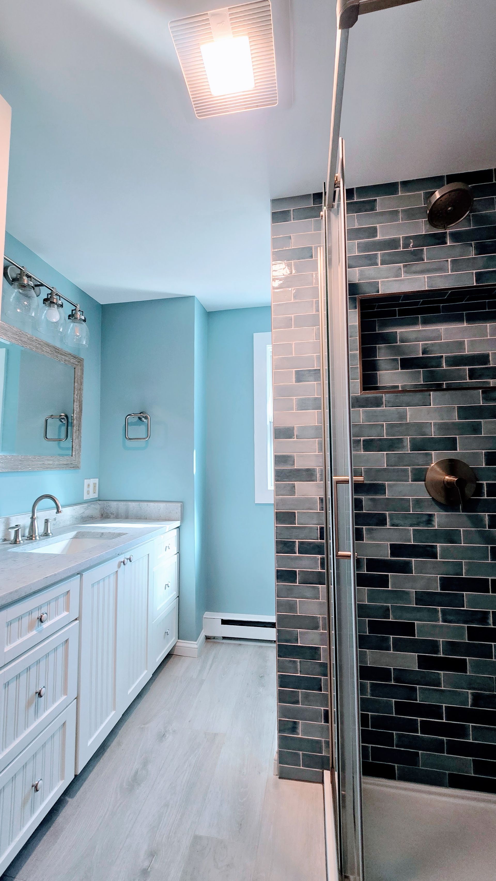 Bathroom remodel in Ashford, CT completed by First Choice Bathroom Remodeling with blue walls, white cabinets, gray tile shower, and silver fixtures.