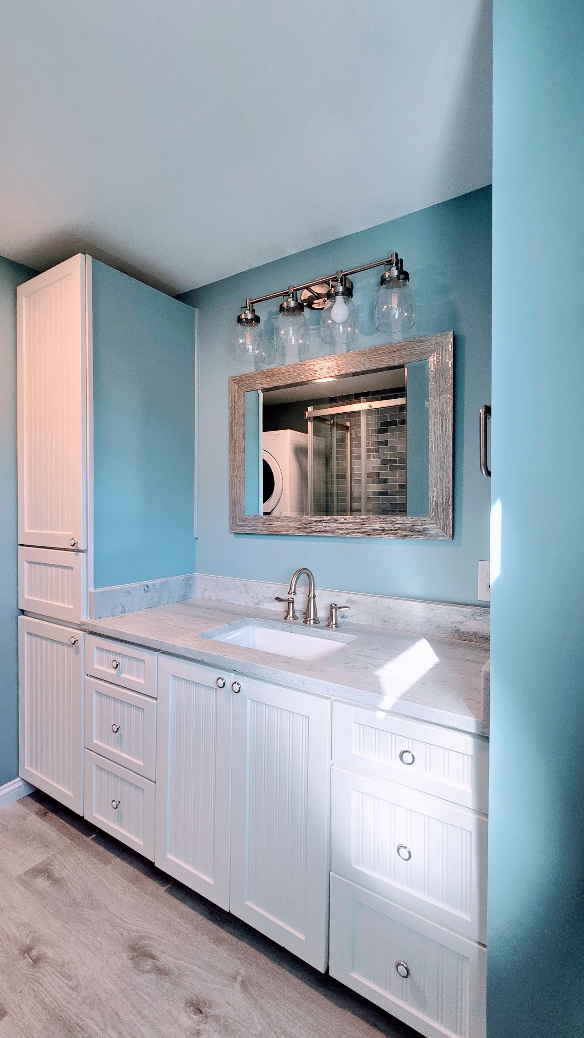 Bathroom remodel in Ashford, CT completed by First Choice Bathroom Remodeling with white cabinets, blue walls, a marble countertop, and a large mirror.