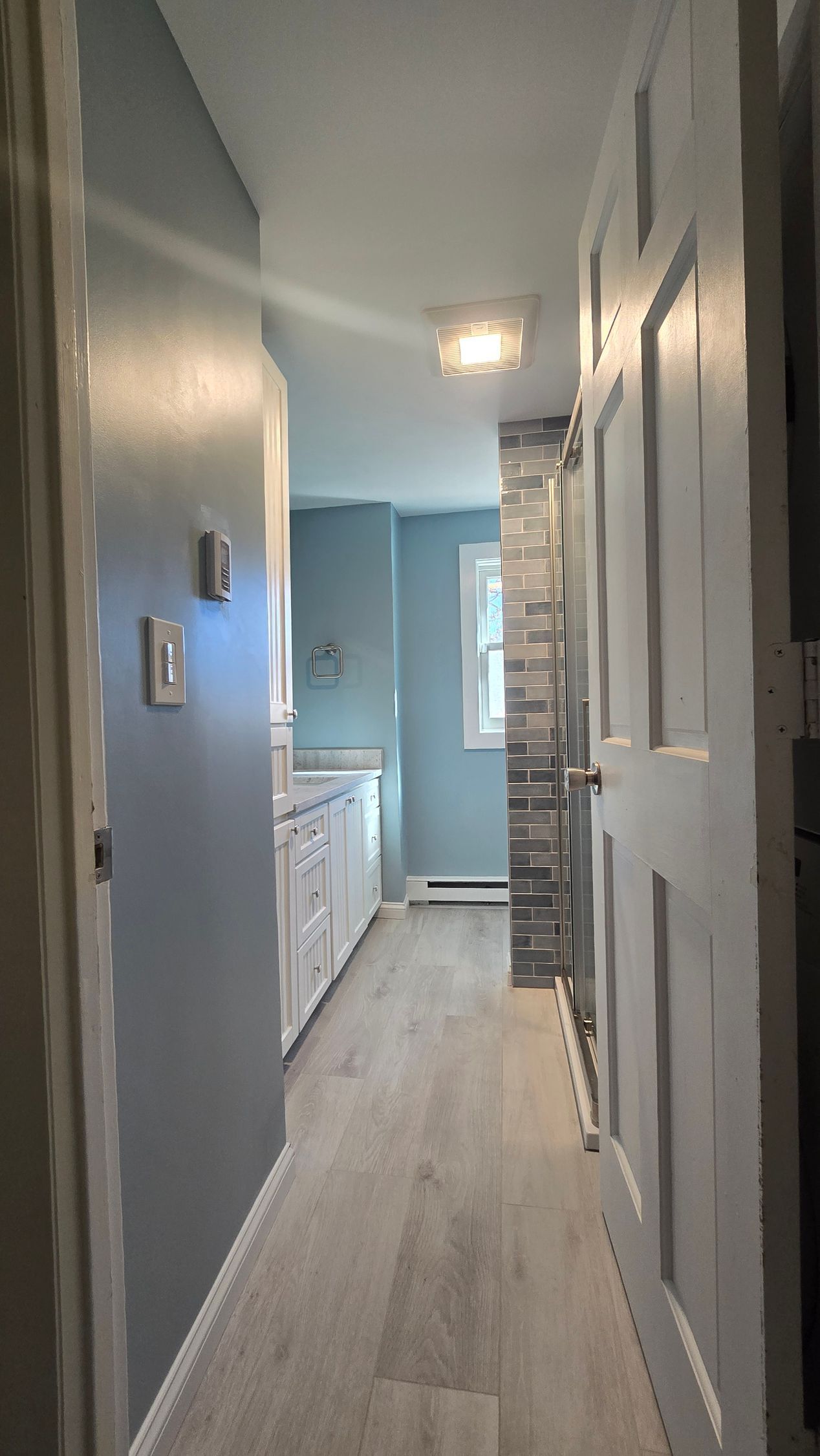 Bathroom remodel in Ashford, CT completed by First Choice Bathroom Remodeling with Narrow hallway with light gray floor, light blue walls, white cabinets, and white doors.