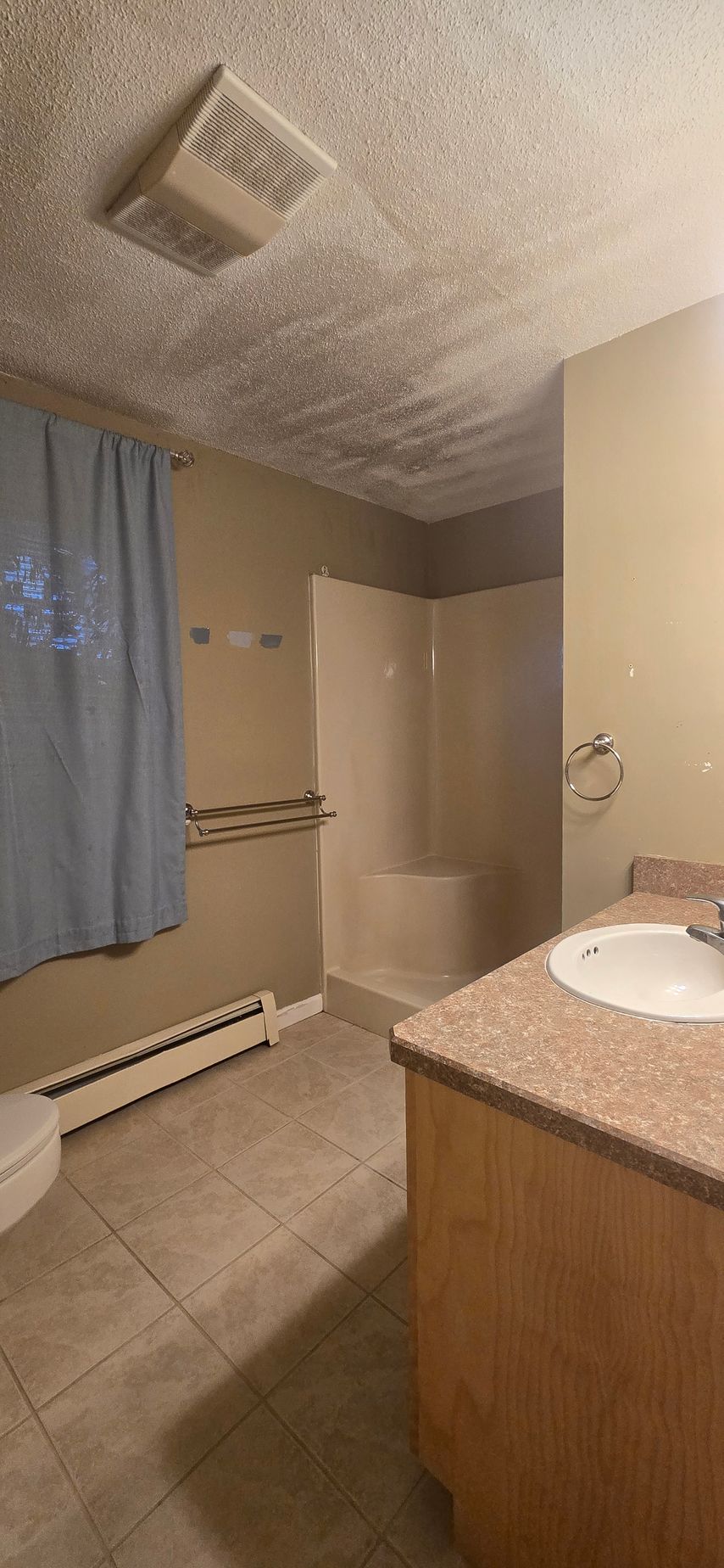 Bathroom with a sink, shower, toilet, and blue curtain. The ceiling has a textured popcorn finish.