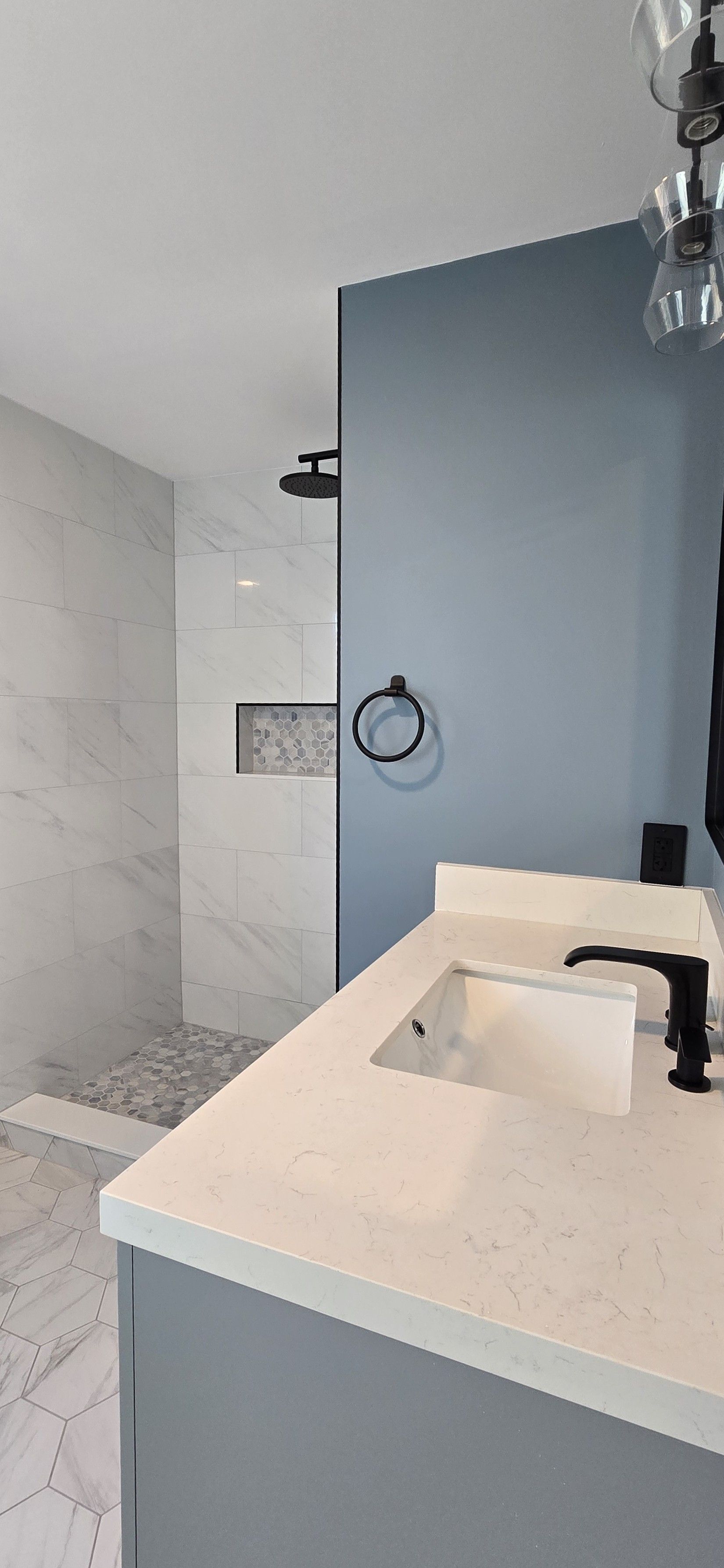 Modern bathroom in Wethersfield, CT with a white countertop and blue wall, shower in the background.