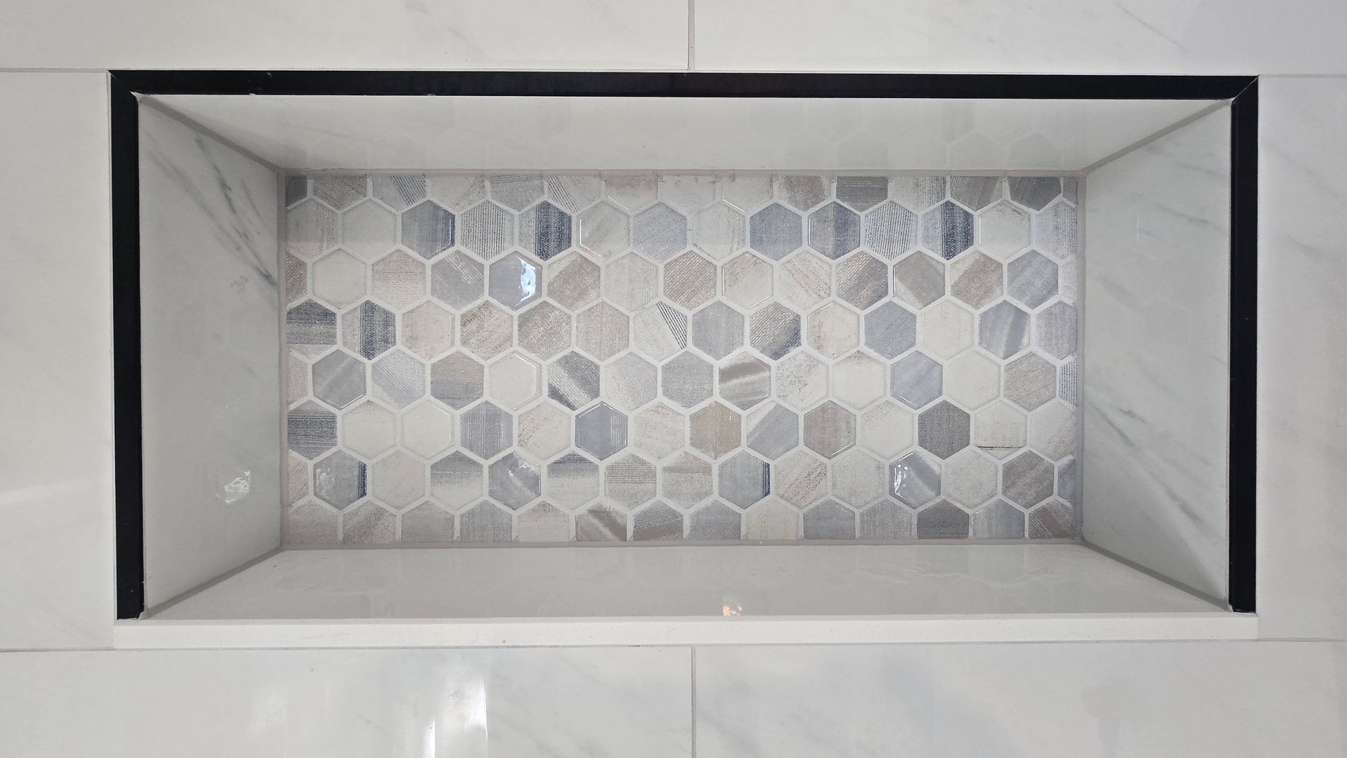 Recessed shower niche in Berlin, CT with honeycomb tile backing and marble-look sides. Black trim around the opening.