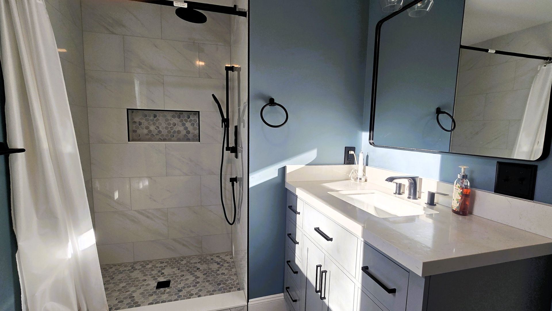 Bathroom with a walk-in shower in Berlin, vanity, and blue walls. Black fixtures, white countertop.