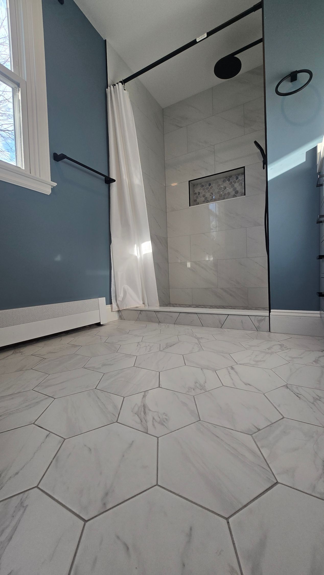 Dark blue bathroom vanity in Wolcott, CT  with gold fixtures, arched mirrors, and marble tile shower.