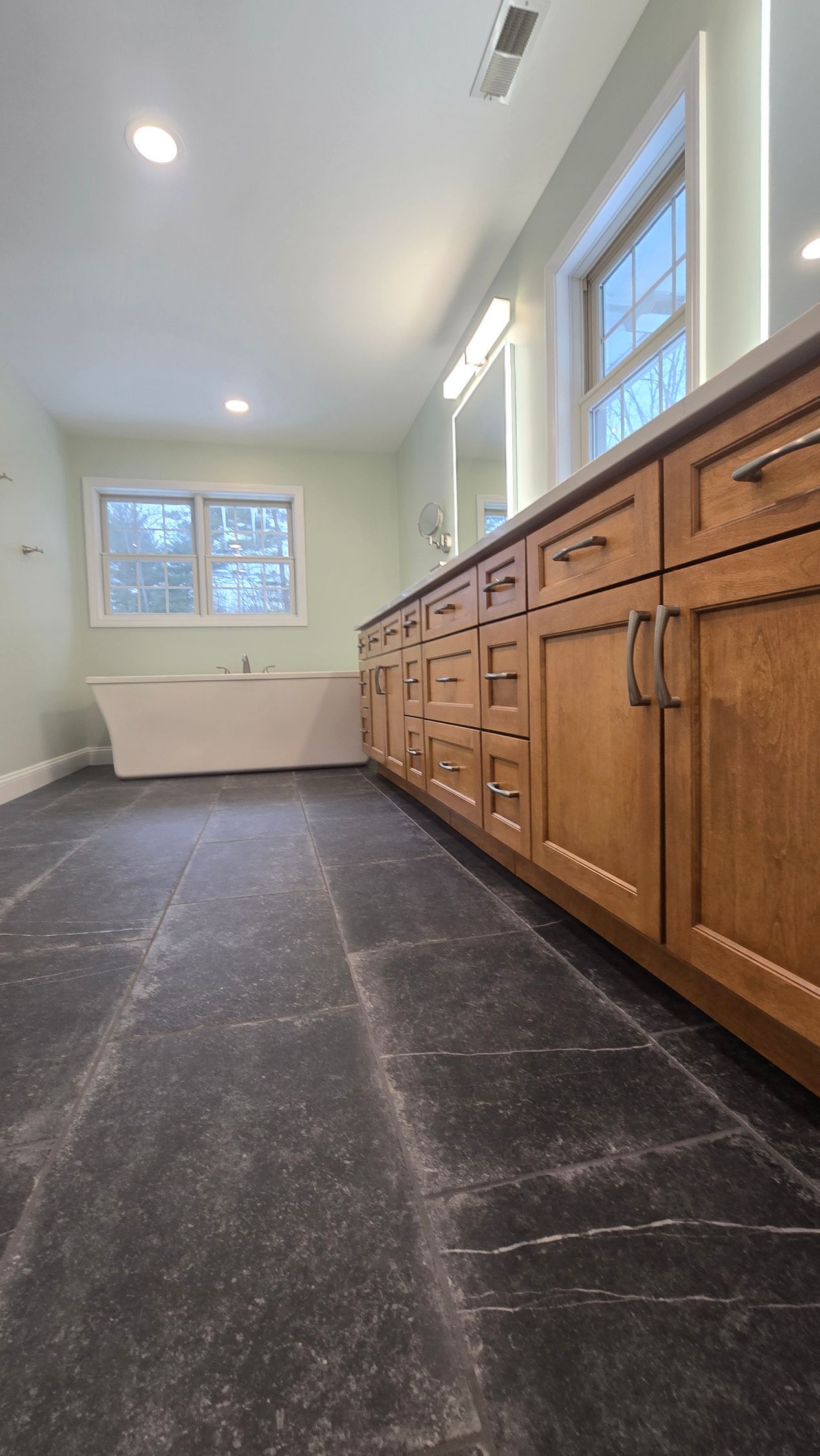 Bathroom with dark floor in Glastonbury, CT, light green walls, wooden cabinets, and a window.