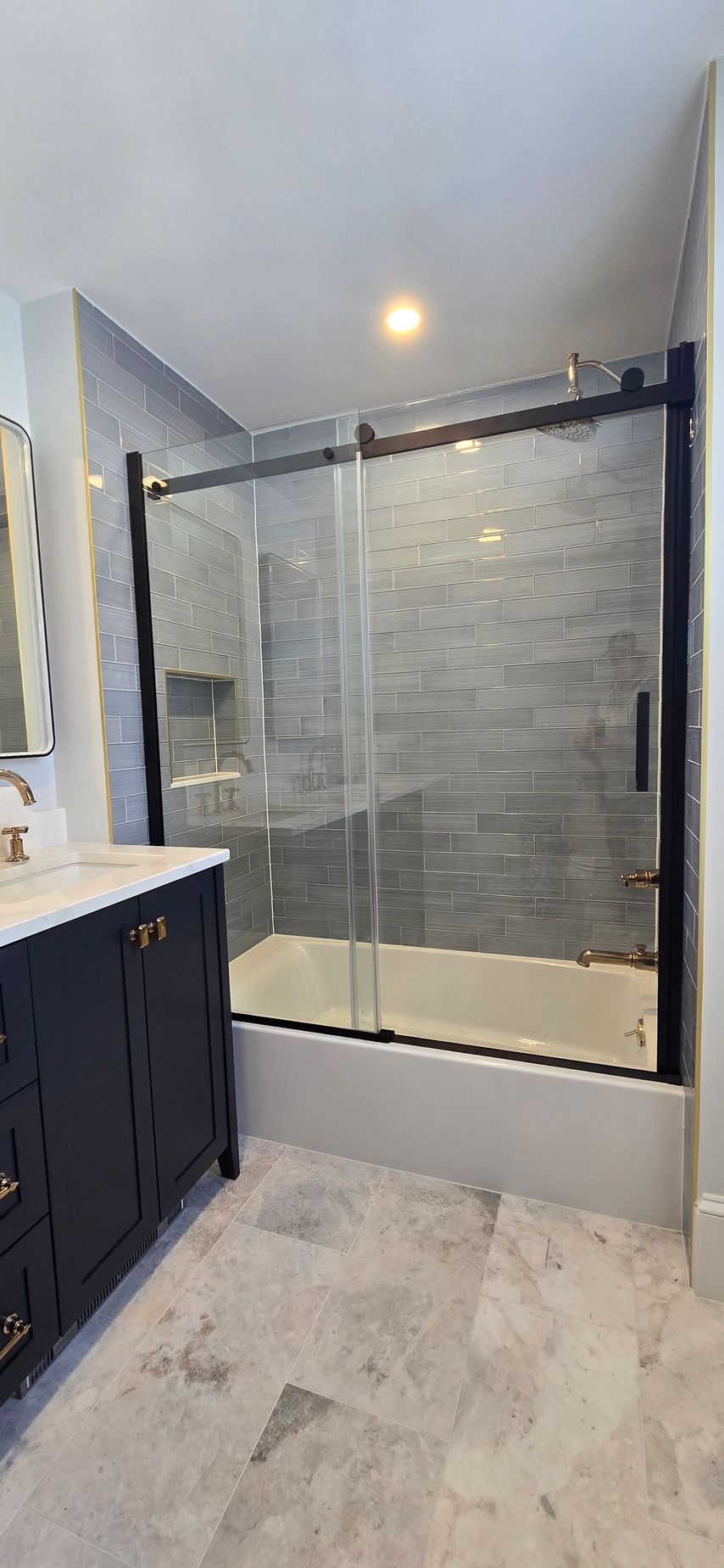 Bathroom with dark blue vanity, grey tile floor, and a glass shower door with black framing.