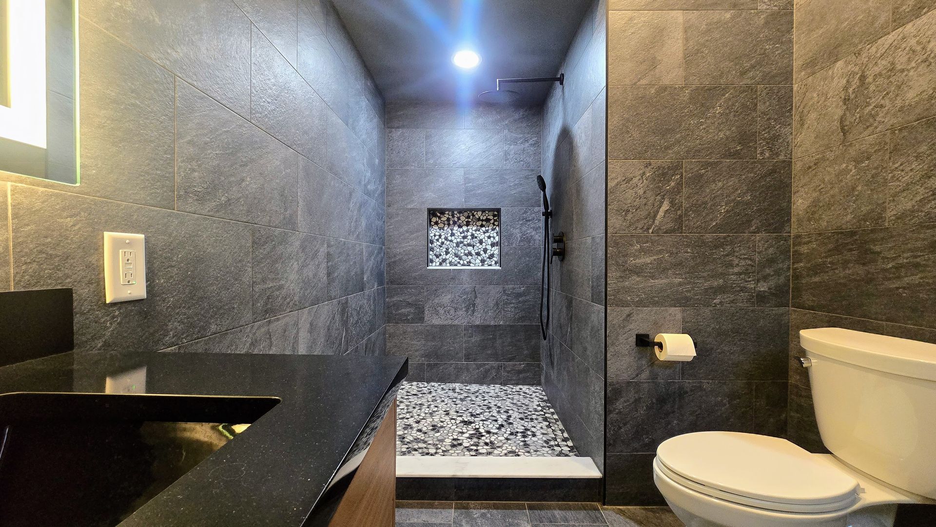 Bristol bathroom with white tub, speckled tile wall, black shower fixtures, and a recessed shelf.