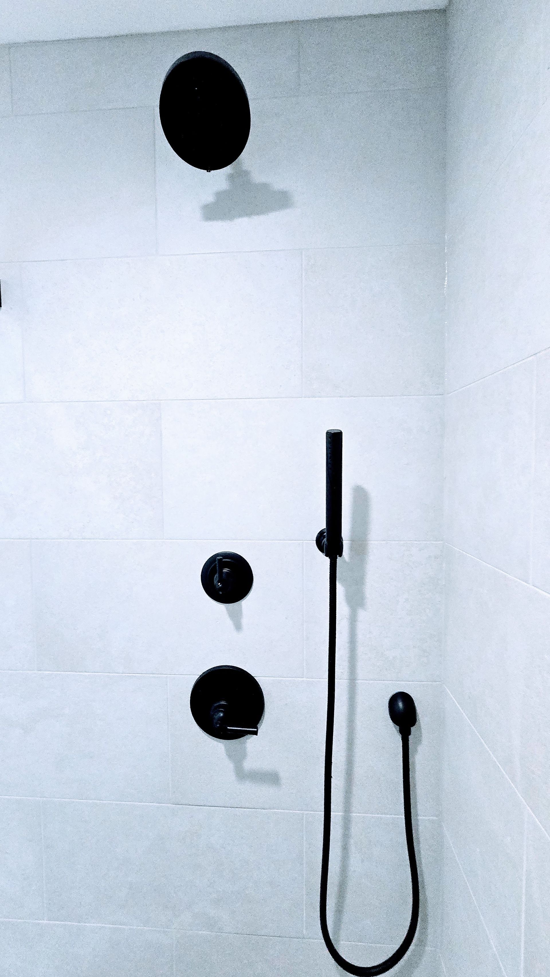 Black shower fixtures in Berlin, CTon white tiled wall. Includes a large showerhead, controls, and hand shower.