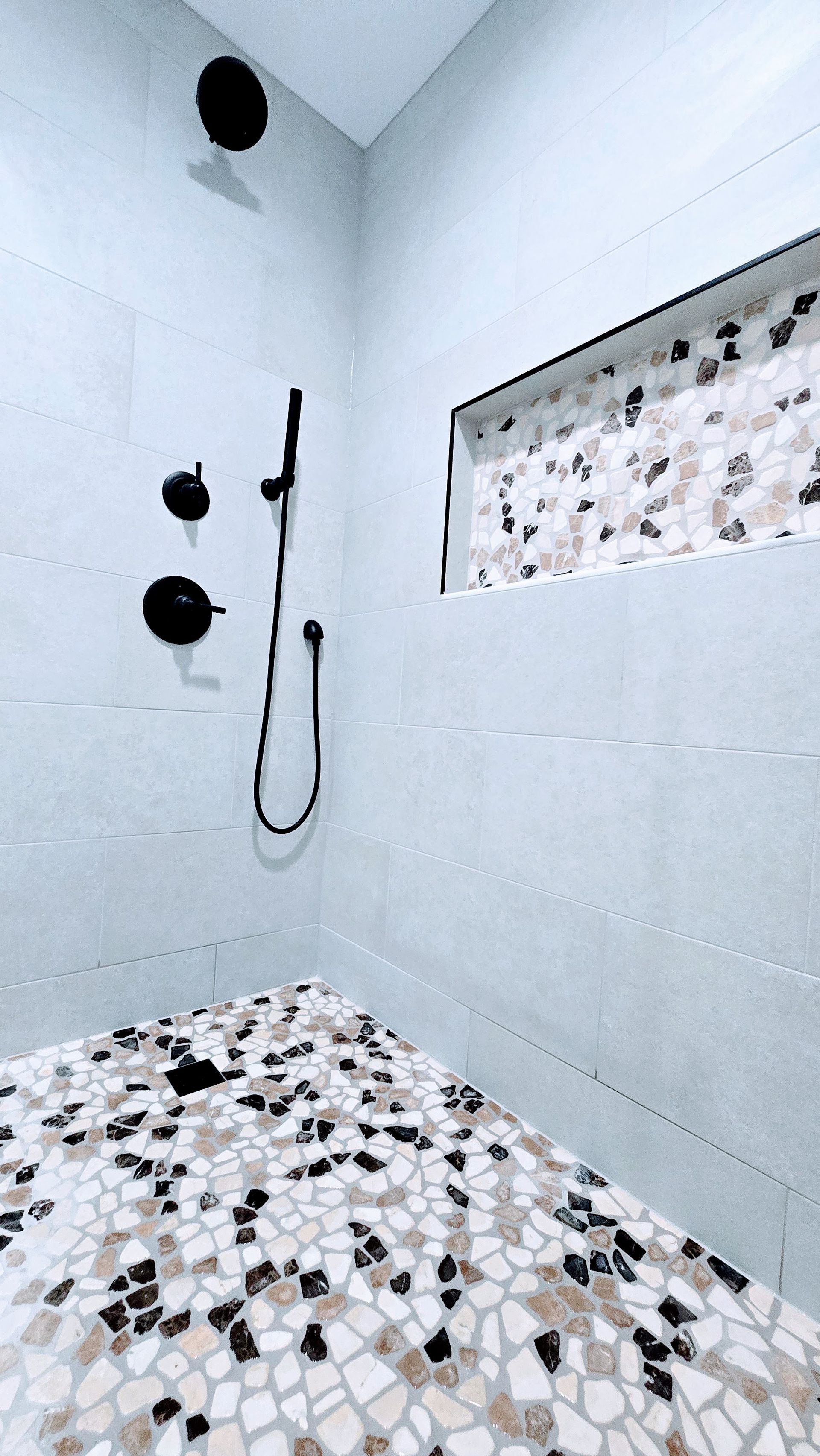 Shower stall in Berlin, CT with light-colored stone tile walls and a mosaic tile floor with brown and black accents.