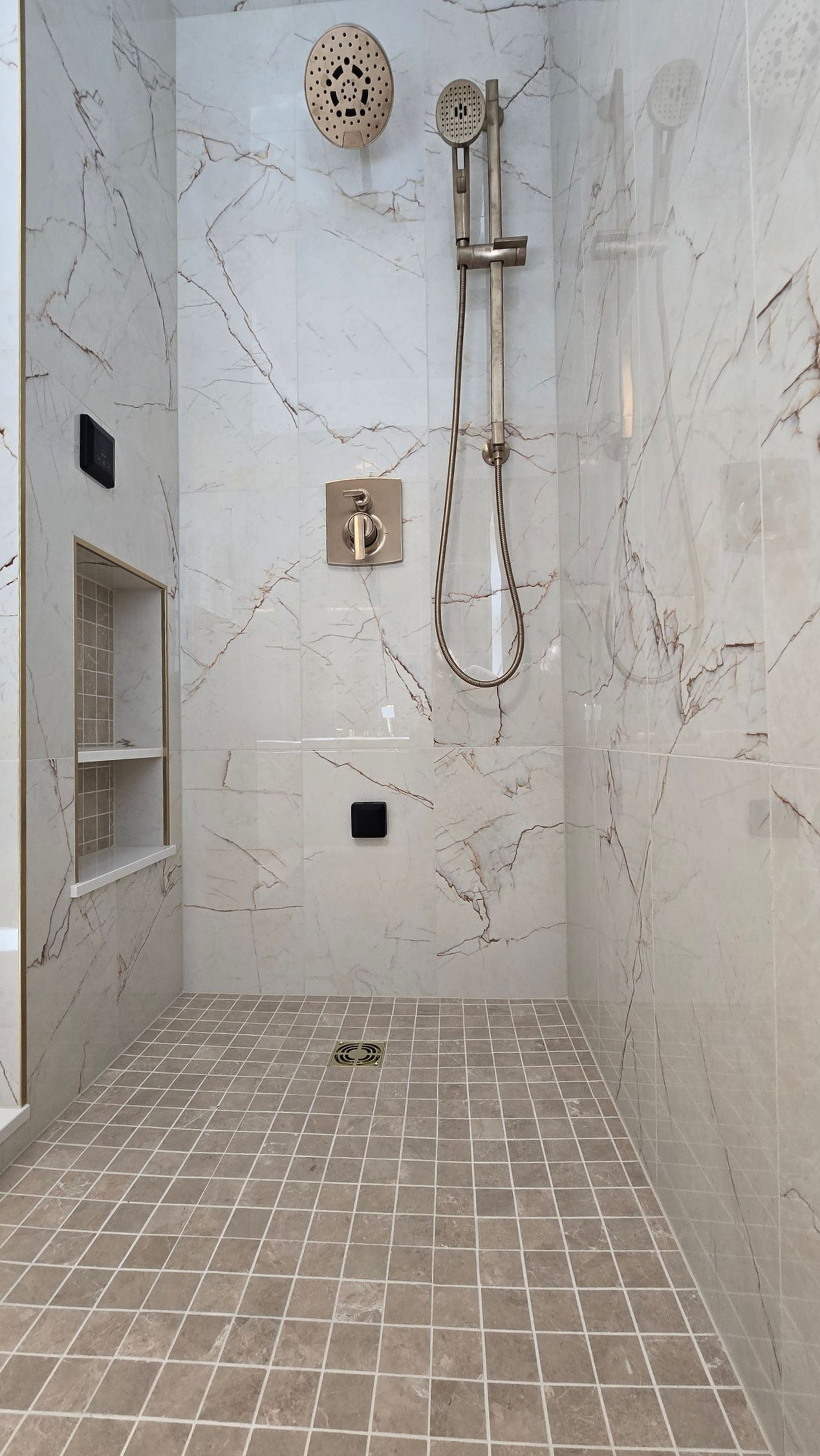 A walk-in shower in Cromwell, CT with light marble-patterned tile walls, a handheld showerhead, a wall-mounted faucet, and mosaic tile floor.