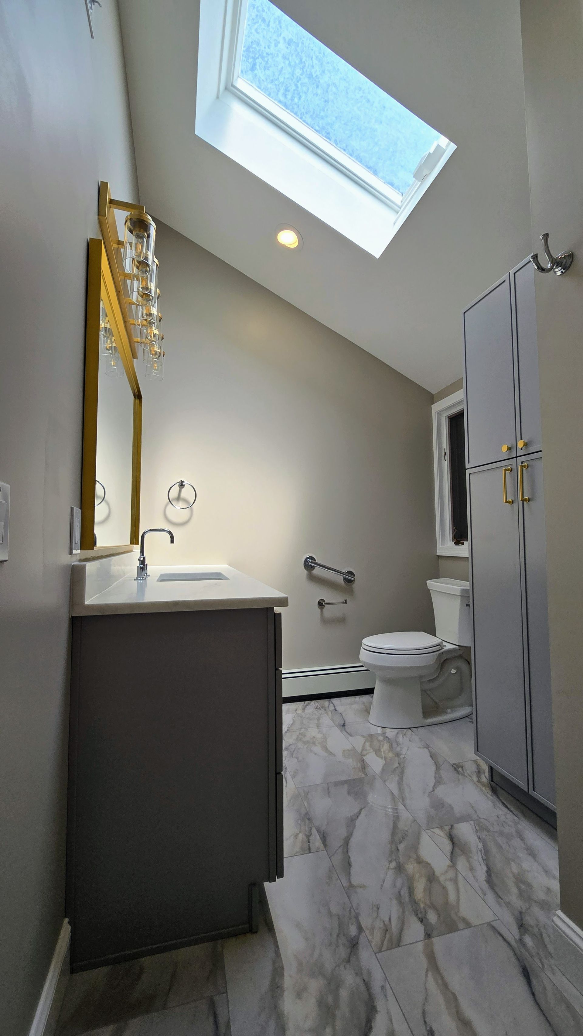 Bright modern bathroom with skylight, white toilet, vanity, and gray marble floor tiles
