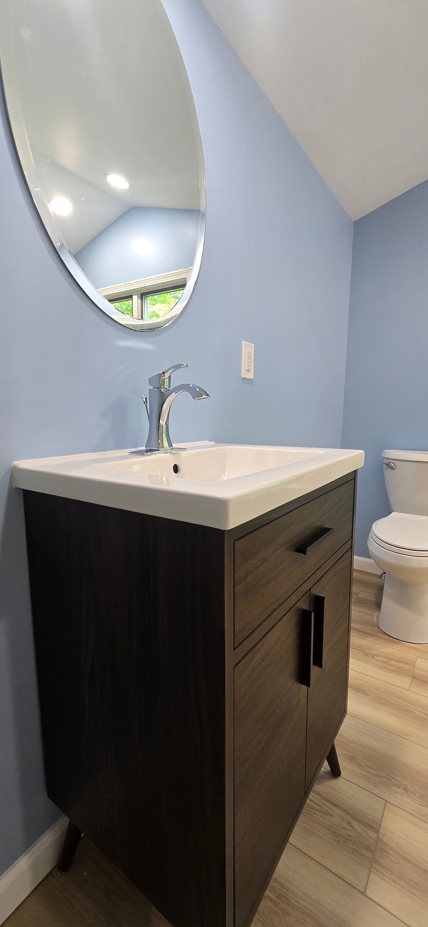 Small bathroom vanity with oval mirror, white sink, and light blue walls