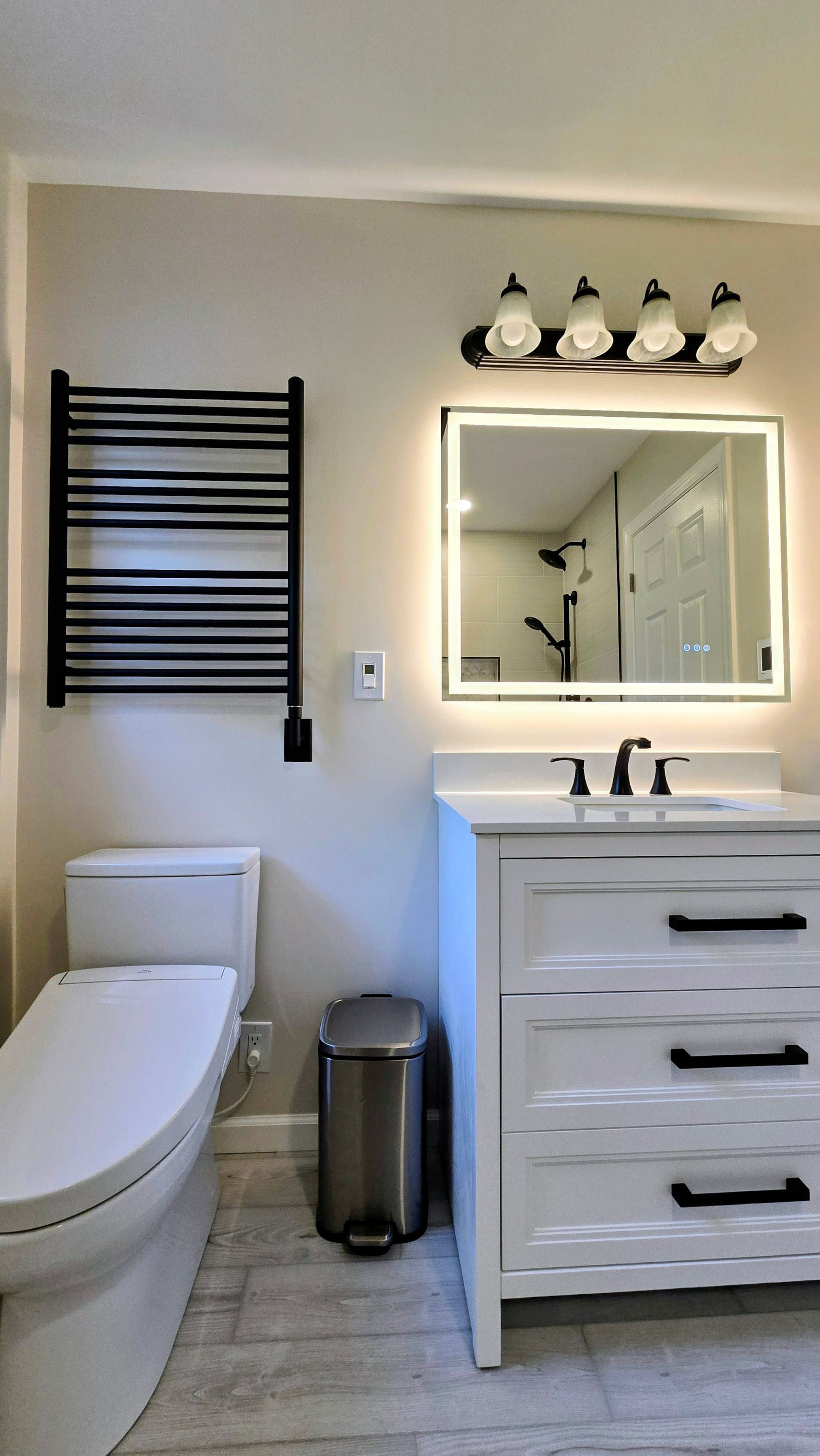 Modern bathroom with toilet, vanity sink, mirror, towel rack, and wall lights