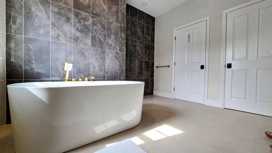 A modern bathroom in Cromwell, CT featuring a white freestanding tub against a dark, industrial-style tiled wall and two white doors.