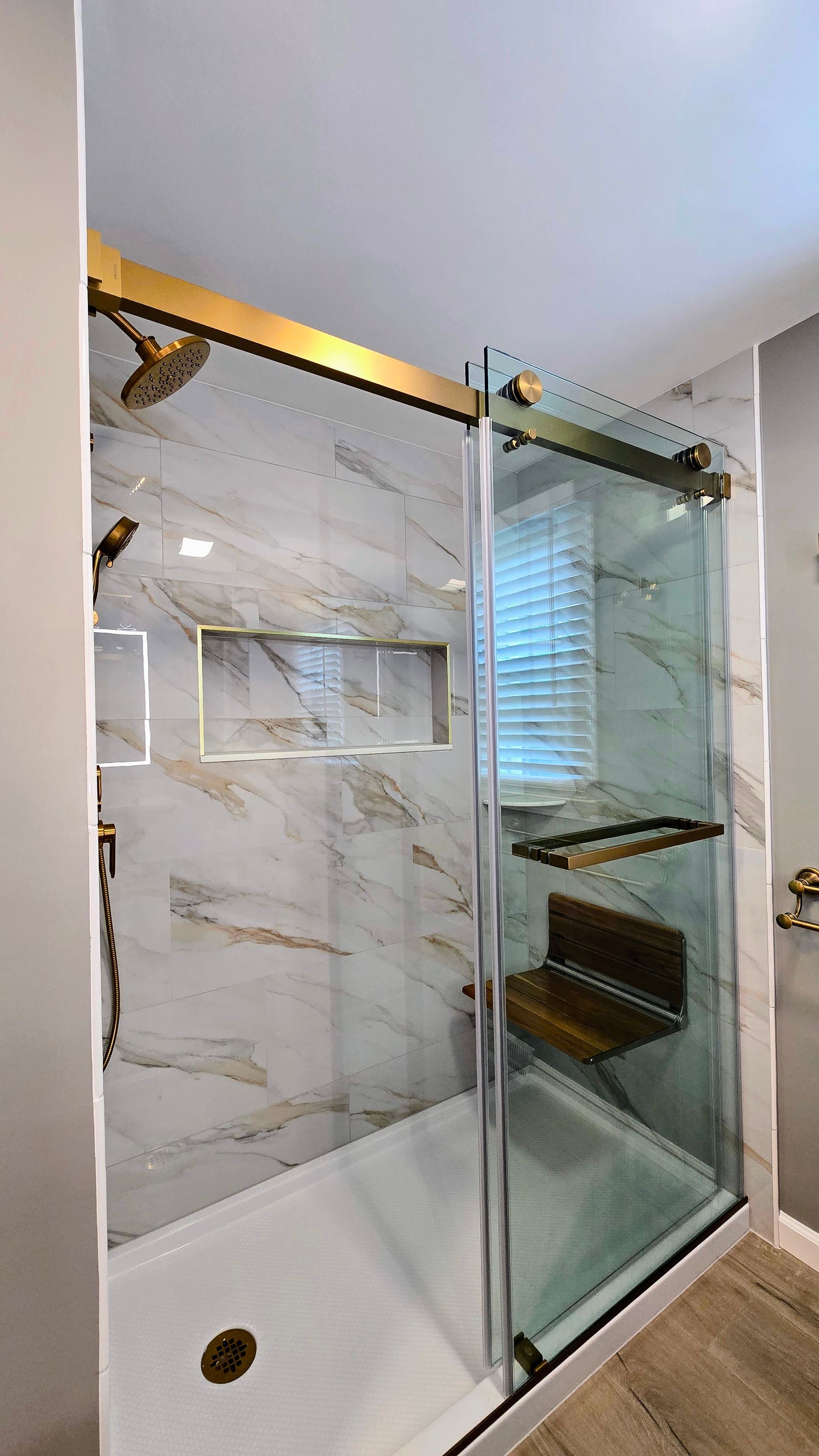 Modern bathroom shower with glass door, marble-look tile walls, and a built-in shelf.