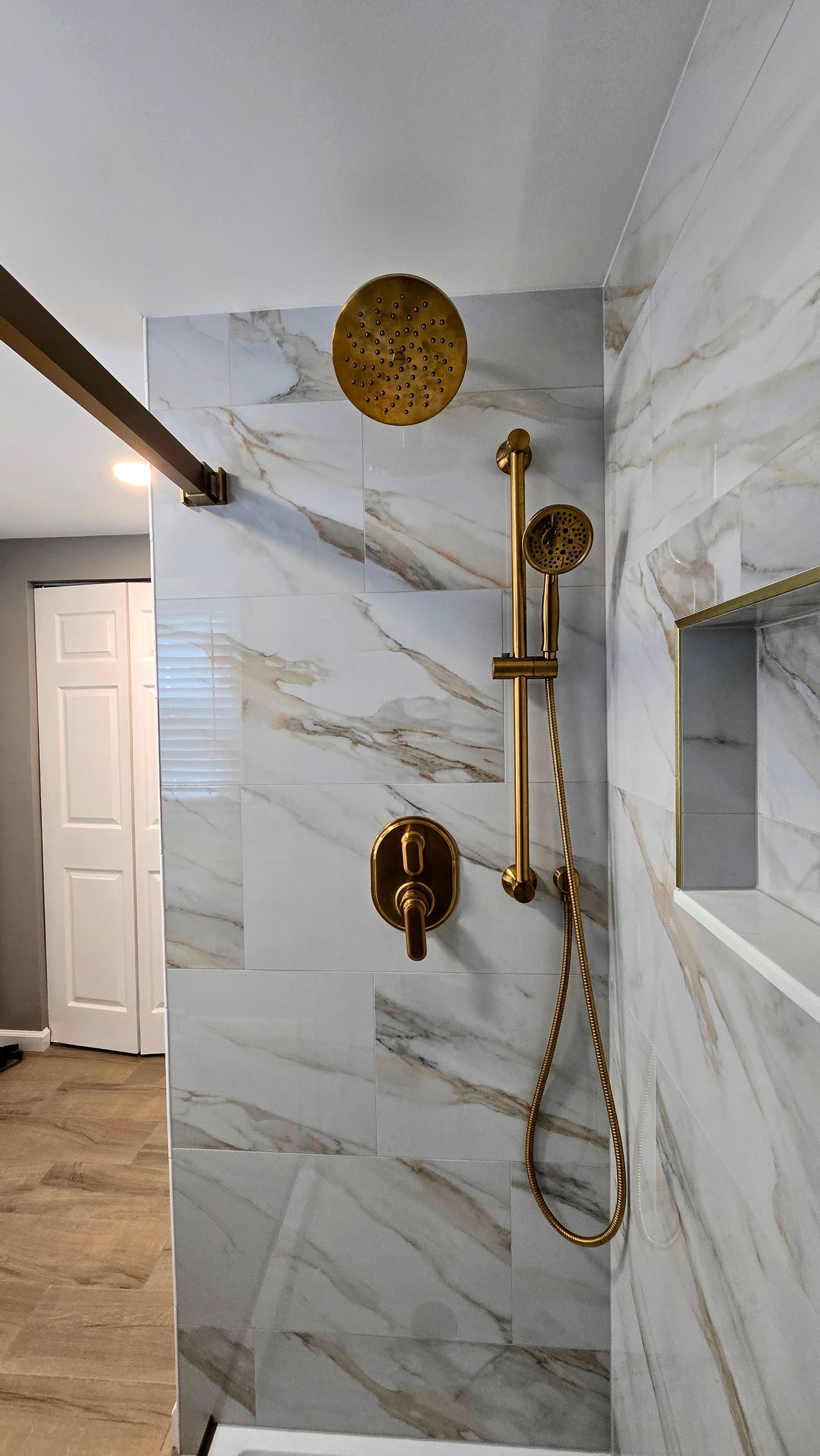 A shower in Simsbury, CT with interior with light gray marble tiles, a circular showerhead, and dual silver control handles on the wall.