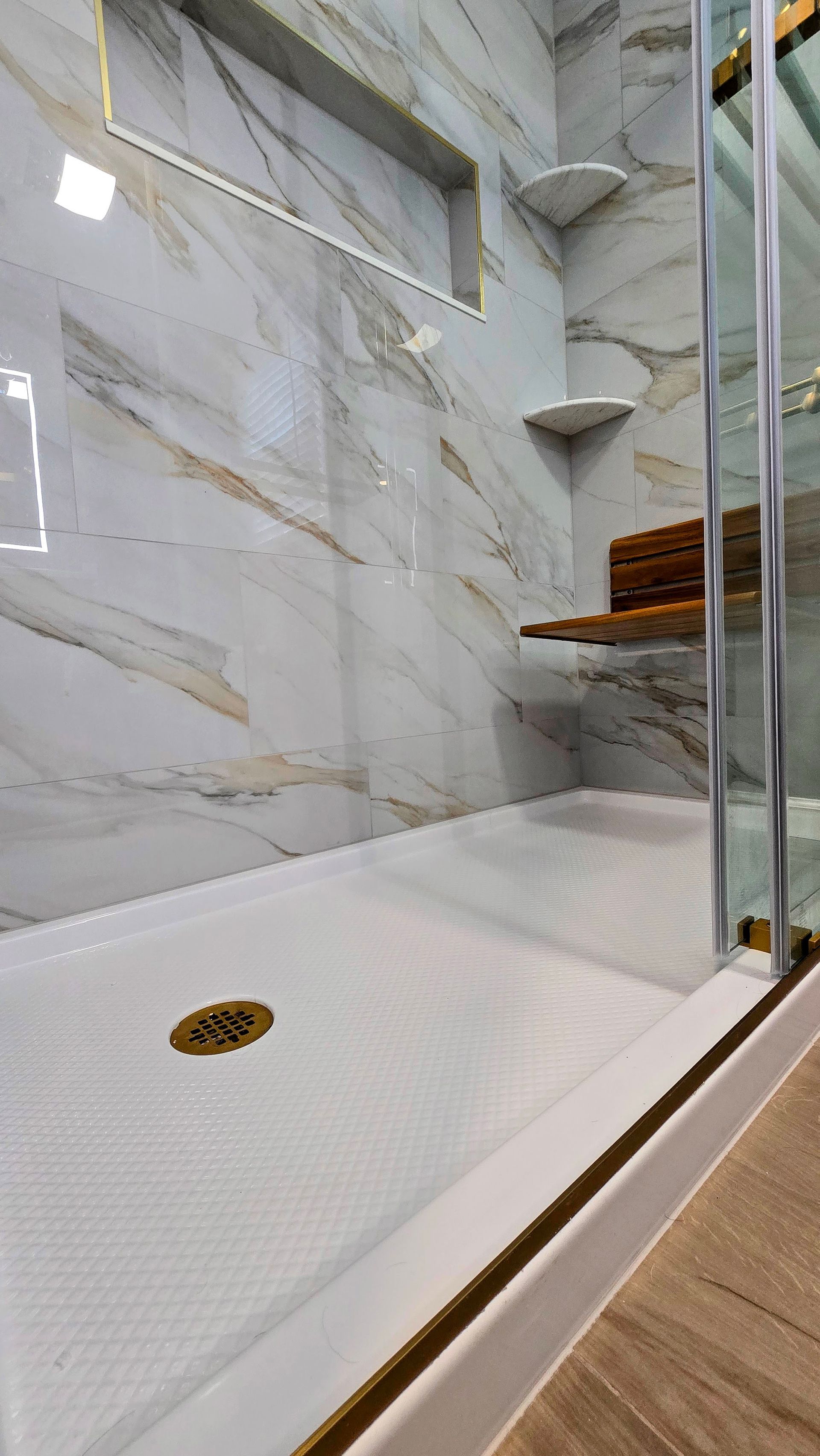 A light-colored stone-tiled shower floor in Simsbury, CT with a single centered chrome shower head.