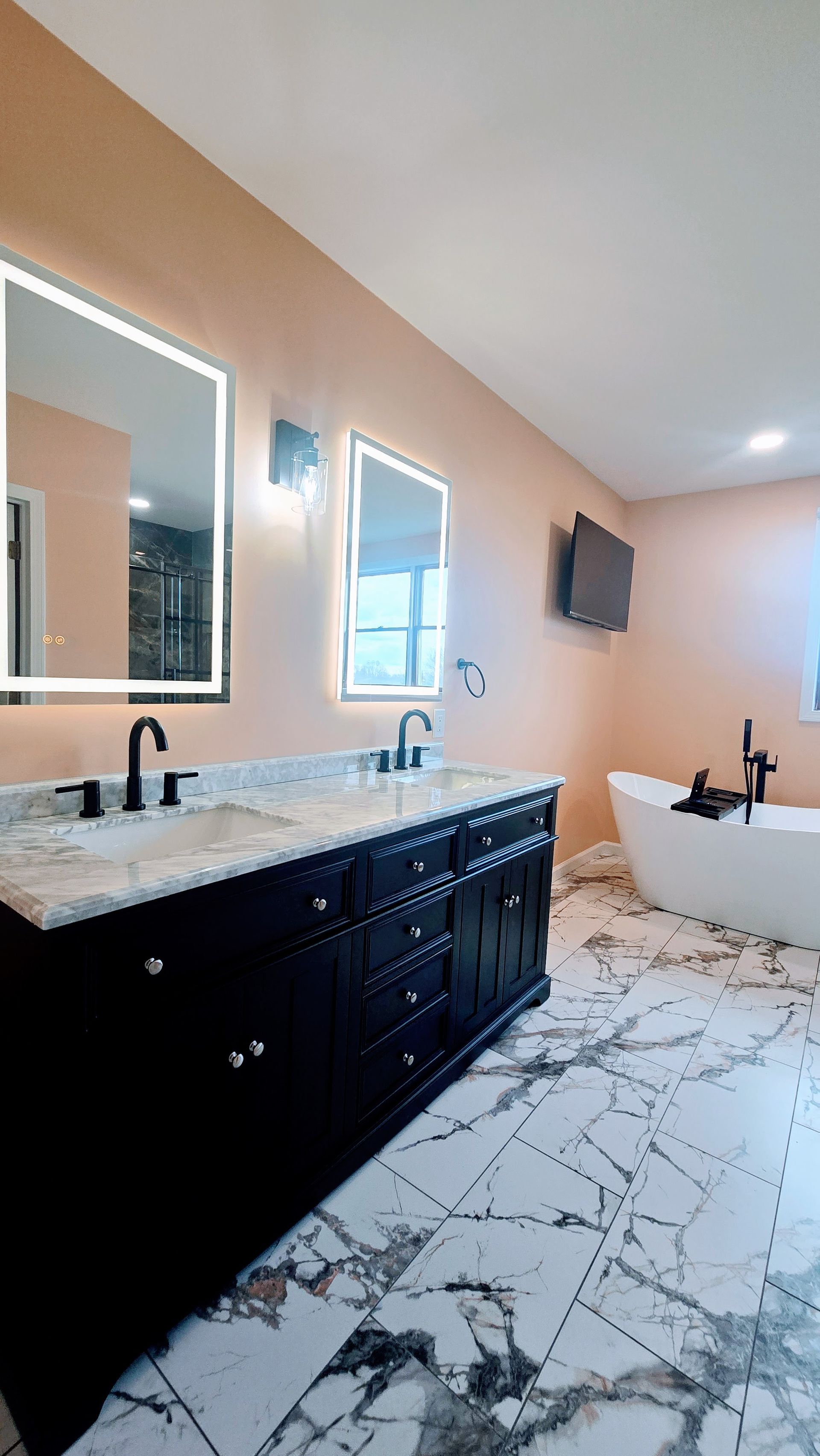 Bathroom in Simsbury, CT completed by First Choice Bathroom Remodeling with black vanity, marble floor, peach walls, and a freestanding tub.