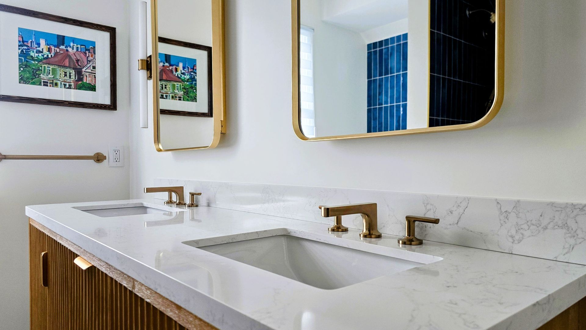 A modern double-sink bathroom vanity in Cromwell, CT with white marble countertops, gold faucets, and rectangular gold-framed mirrors.
