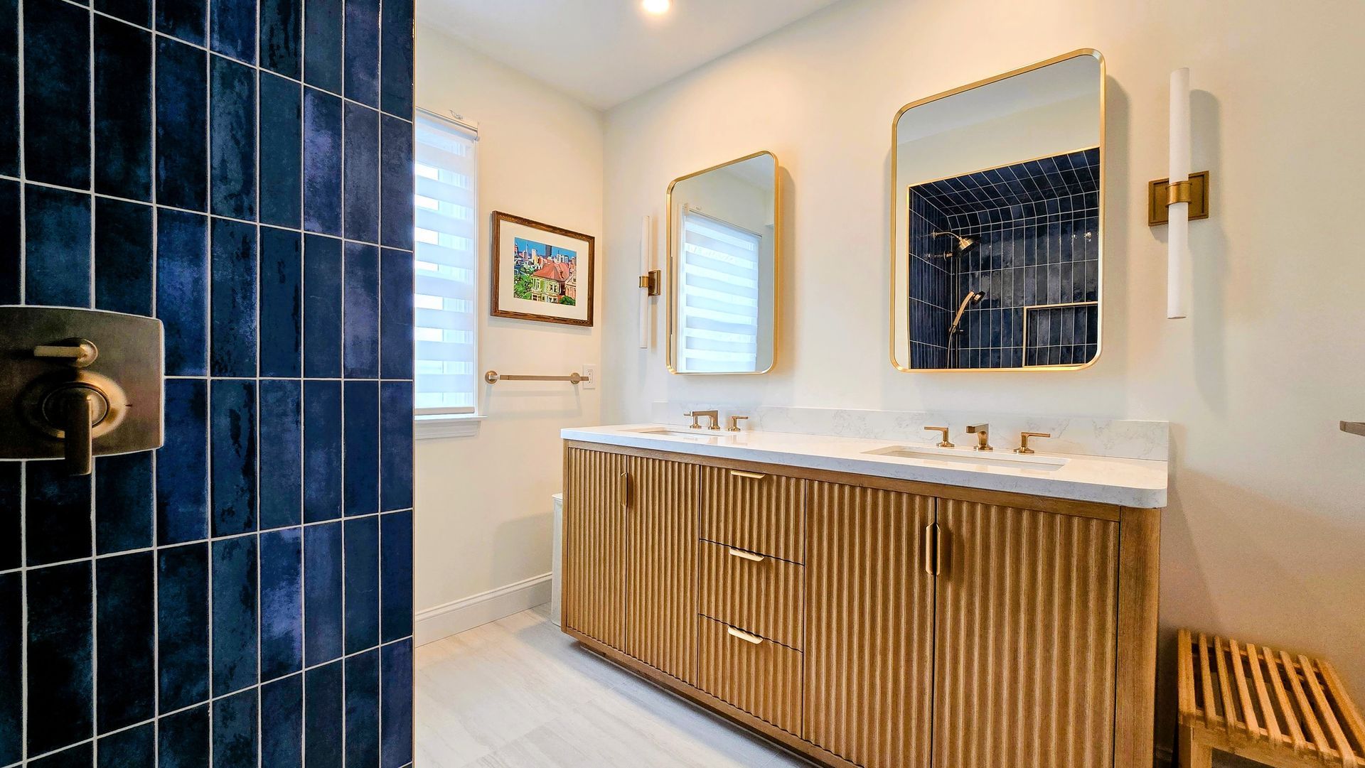 A modern bathroom in Cromwell, CT featuring a double vanity with a wood-slatted front, brass fixtures, and a deep blue tiled shower wall.