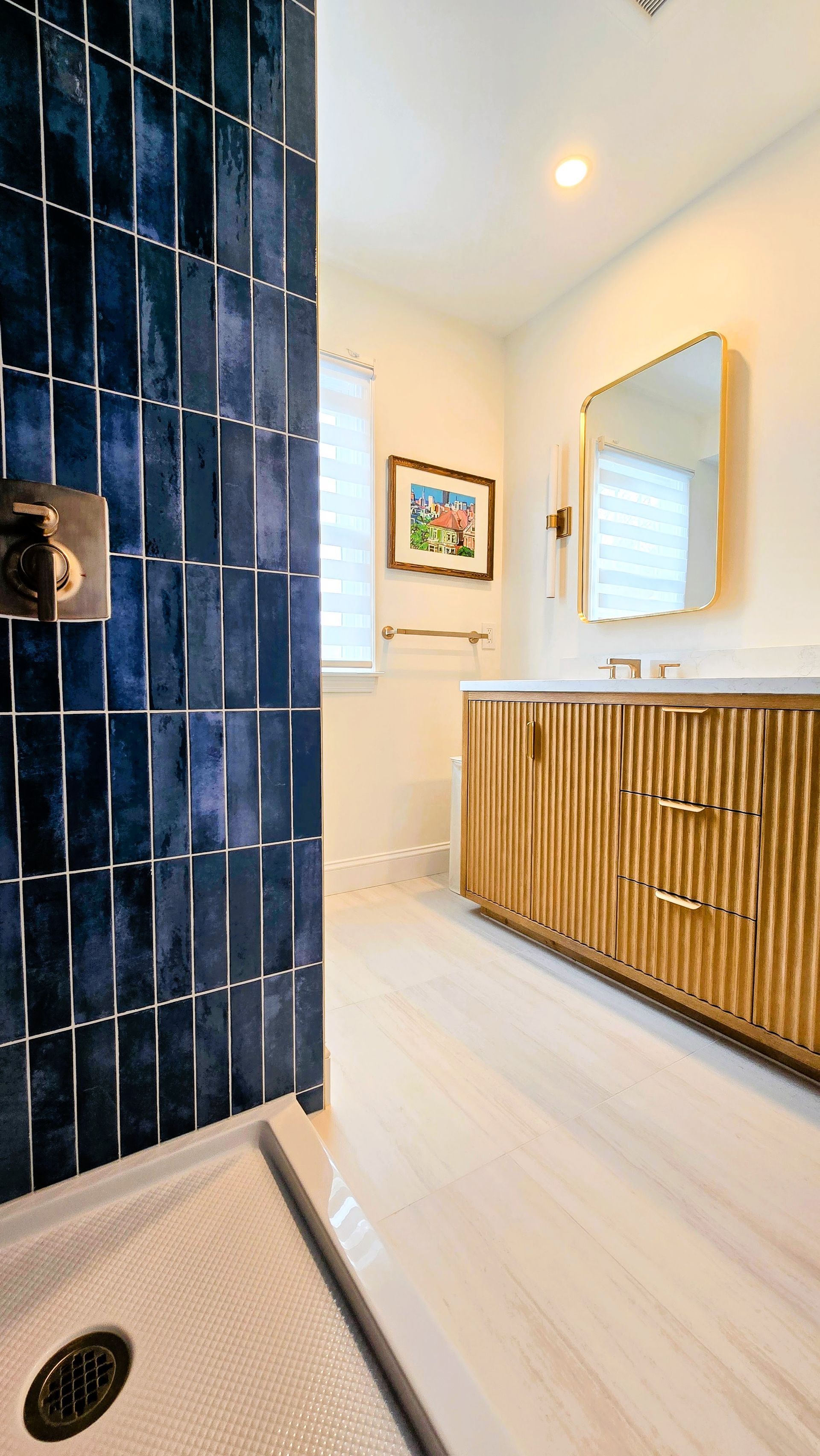 A modern walk-in shower in Cromwell, CT with dark blue vertical tiles, a built-in recessed shelf, and gold hardware.