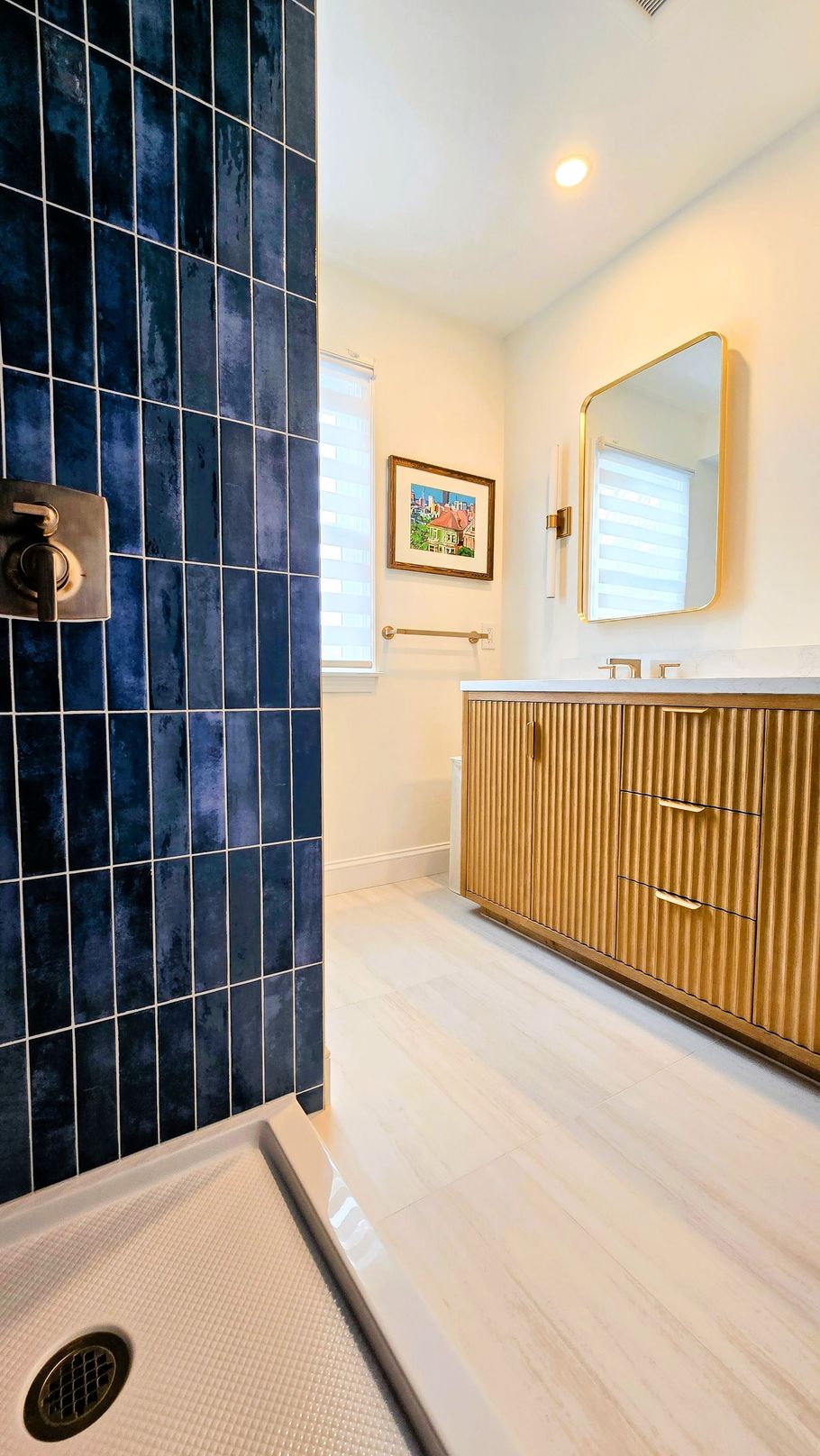 A modern walk-in shower in Cromwell, CT with dark blue vertical tiles, a built-in recessed shelf, and gold hardware.