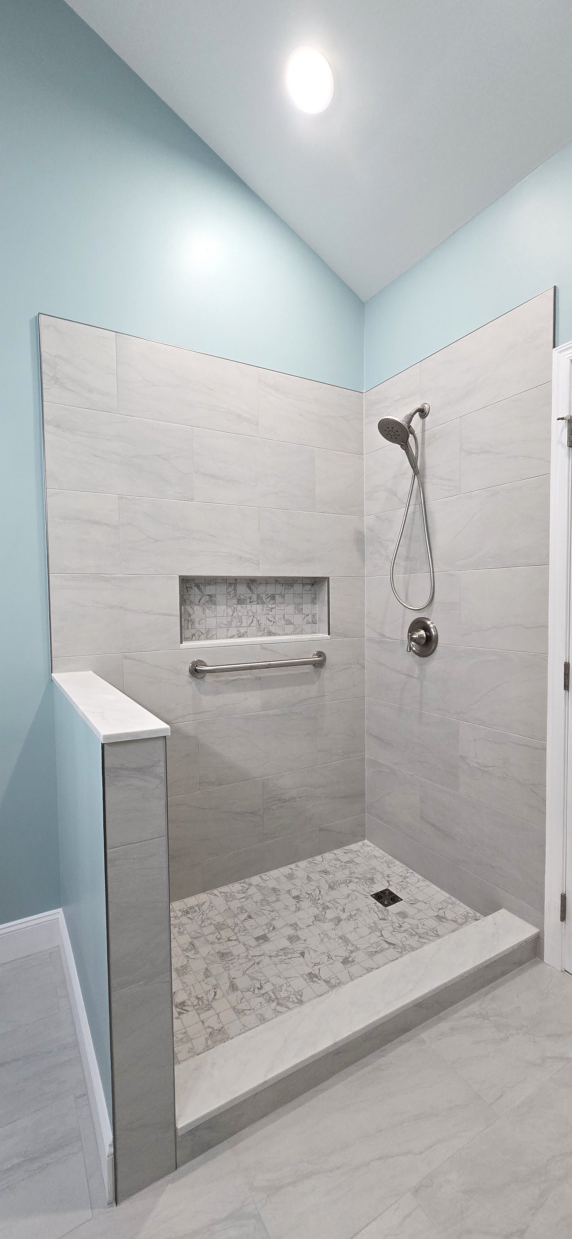 A modern bathroom shower with light gray tiles and light blue walls.