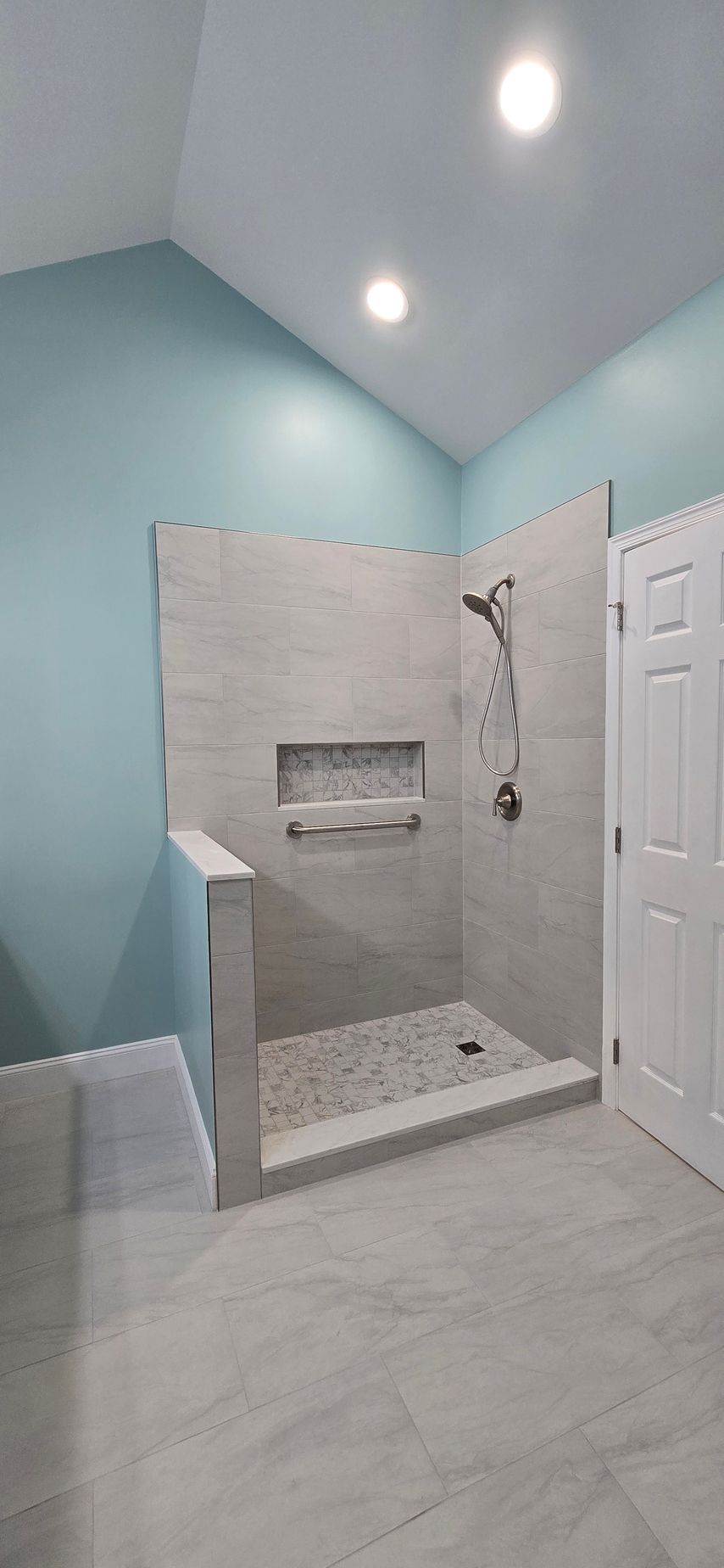 A newly renovated bathroom with a shower. Light blue walls, gray tile, and a pebble-stone shower floor.