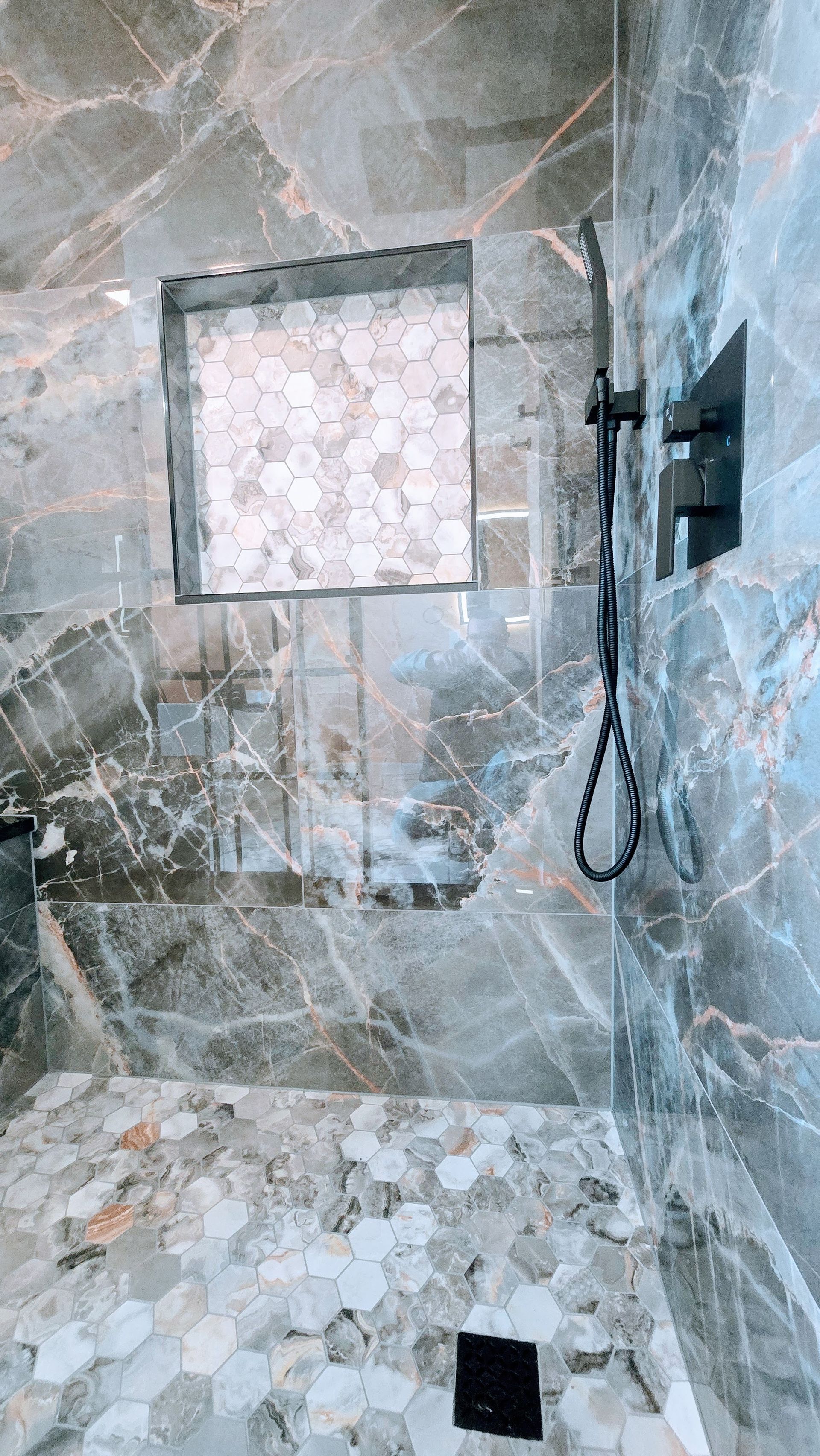 Bathroom Remodel in Seymour, CT completed by First Choice Bathroom Remodeling. Modern shower with a black grid door and marble-look wall. Bright lights overhead.