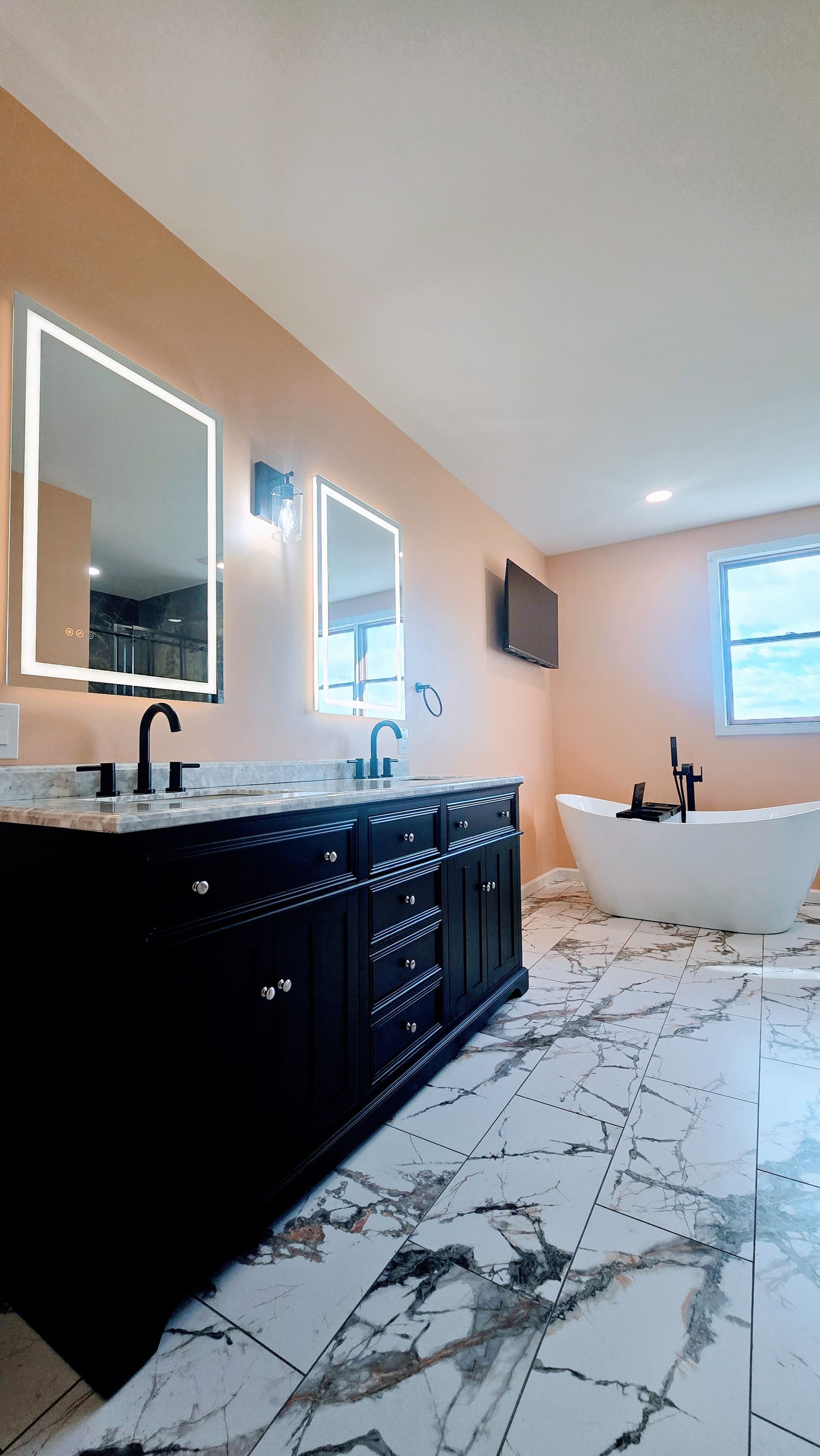 Bathroom Remodel in Seymour, CT completed by First Choice Bathroom Remodeling. Elegant bathroom with black vanity, marble floors, freestanding tub, and illuminated mirrors.