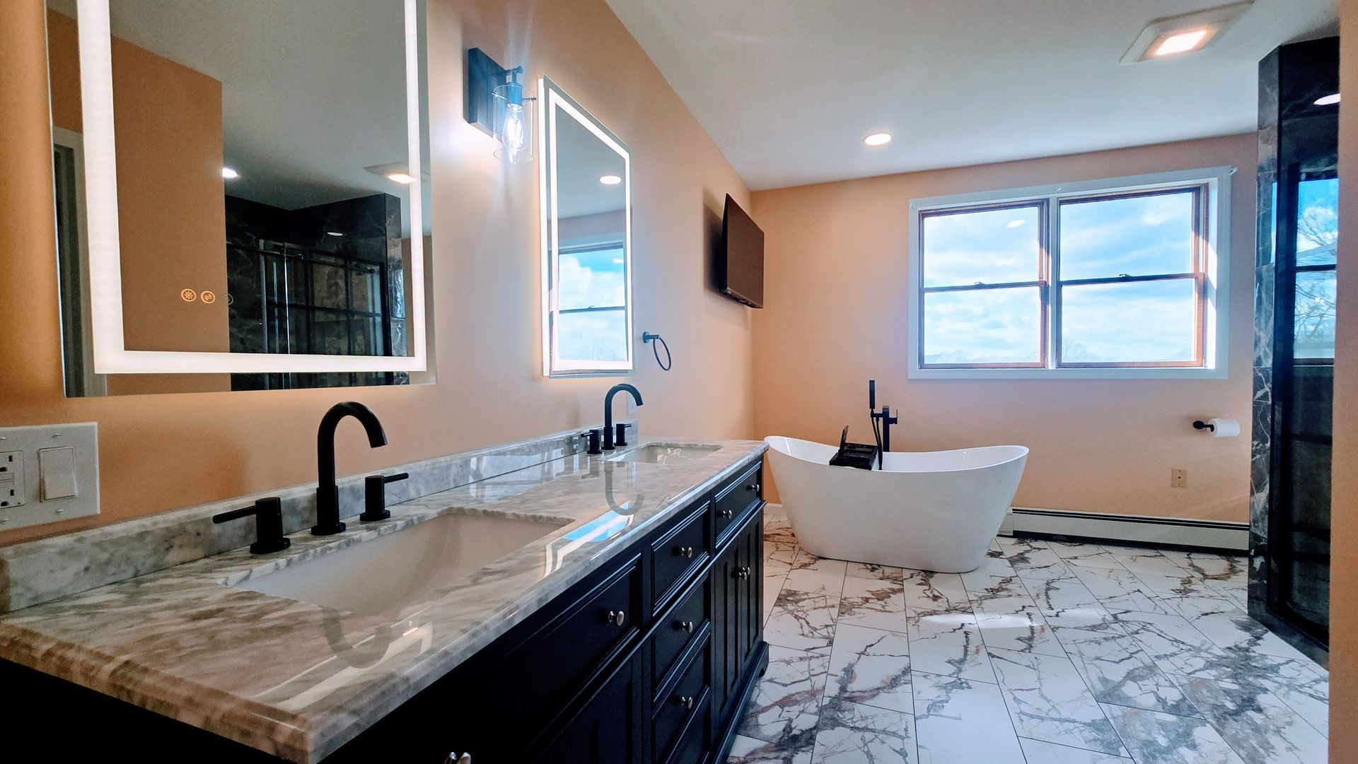 Bathroom with double vanity, soaking tub, large mirrors, black fixtures, and marble flooring.
