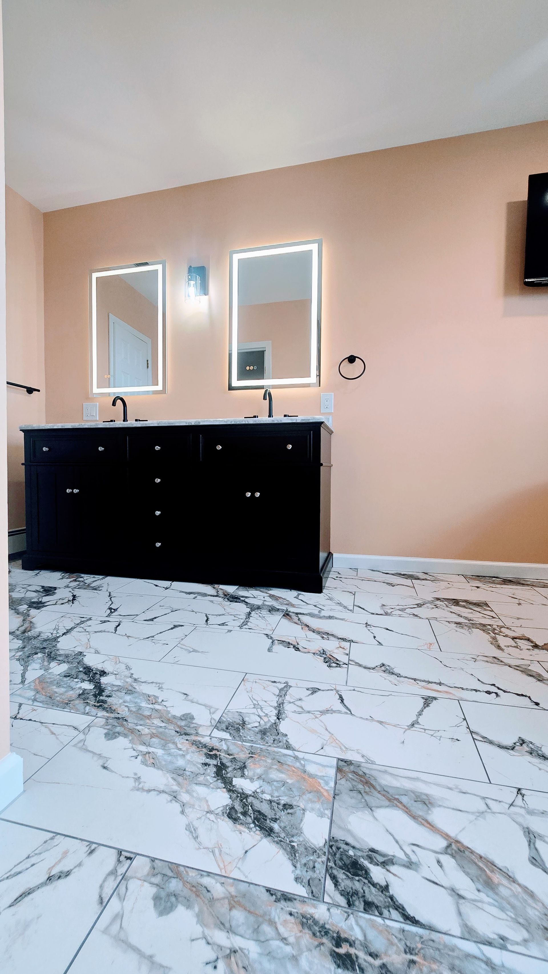 Bathroom Remodel in Seymour, CT completed by First Choice Bathroom Remodeling with black vanity, marble floor, peach walls, and lit mirrors.