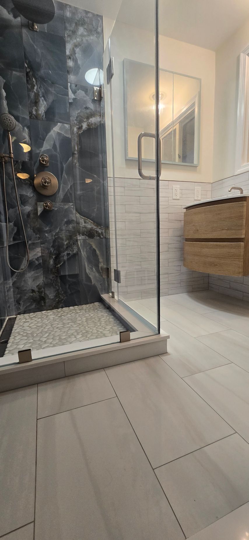 Modern bathroom renovation in Glastonbury, CT with a glass shower, marble shower wall, and wood vanity.