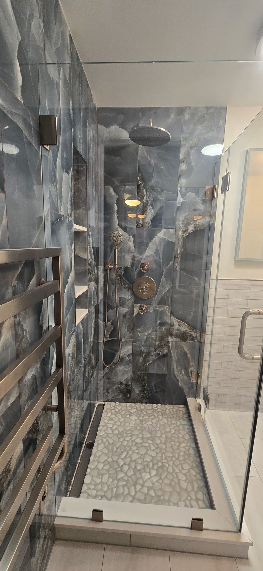 A modern bathroom in Glastonbury, CT with marble walls and a glass-enclosed shower featuring a pebble tile floor.