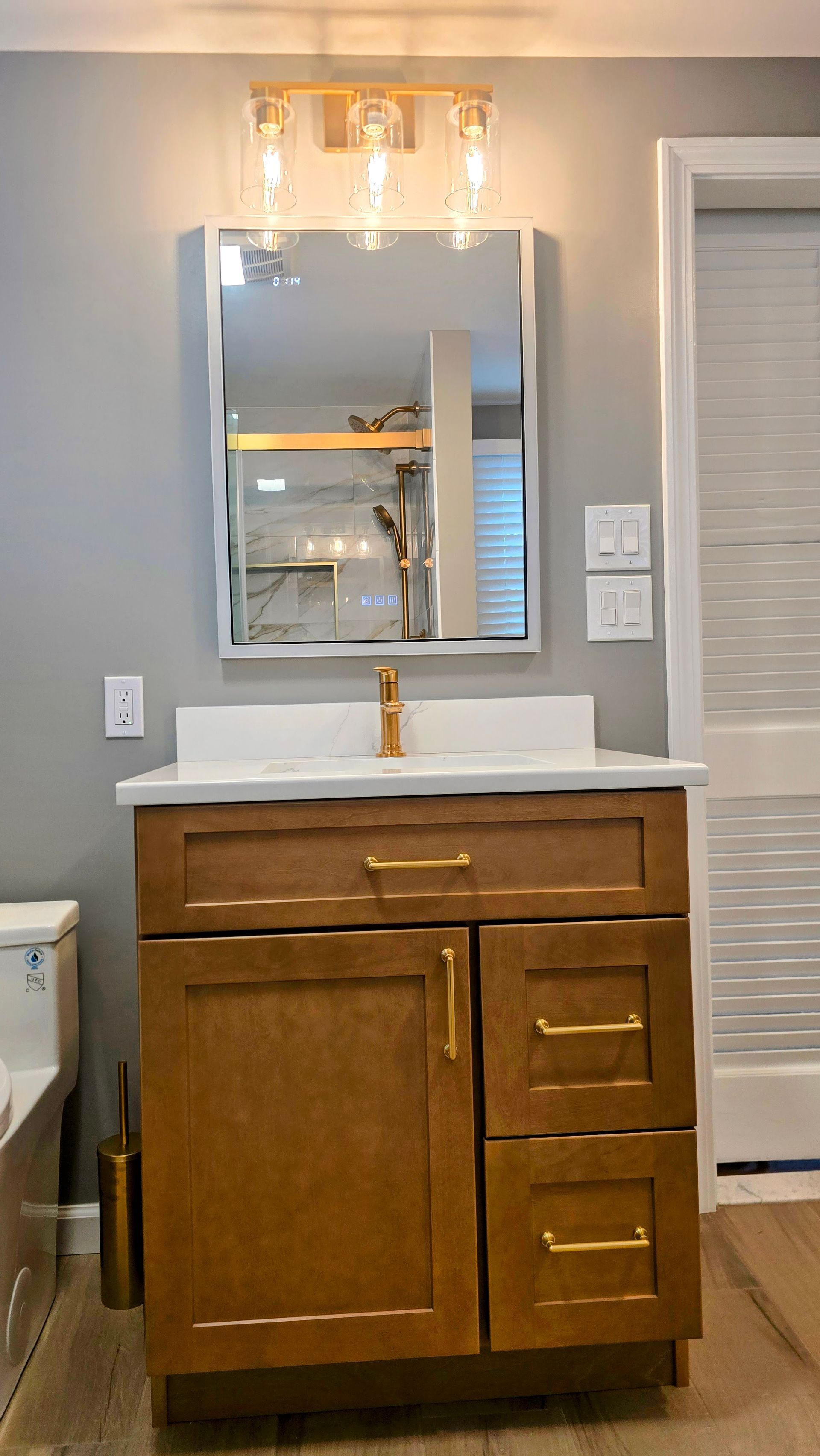 Bathroom vanity with wood cabinet, white sink, mirror, and light fixture above a tiled wall.
