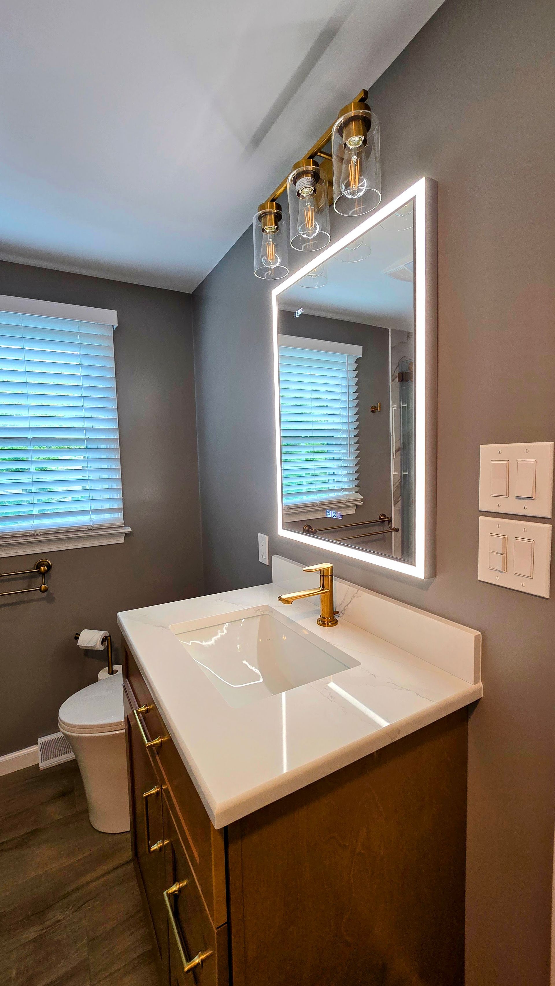 A modern bathroom near Simsbury, CT featuring a white vanity with a glass-shaded wall light, adjacent to a walk-in shower with a glass door.