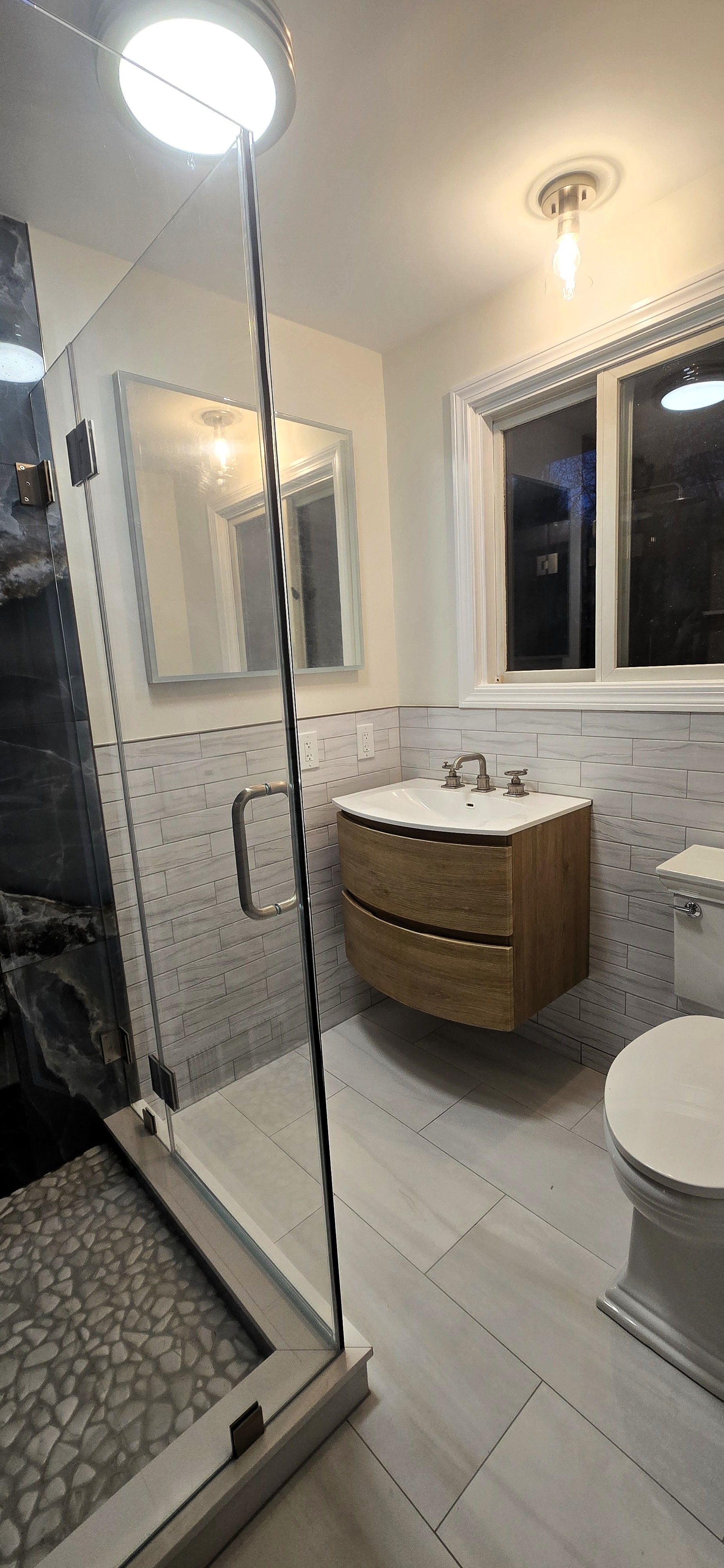 Bathroom remodel in Glastonbury, CT
 with glass shower, floating vanity, toilet, and window. White tile and wood tones.