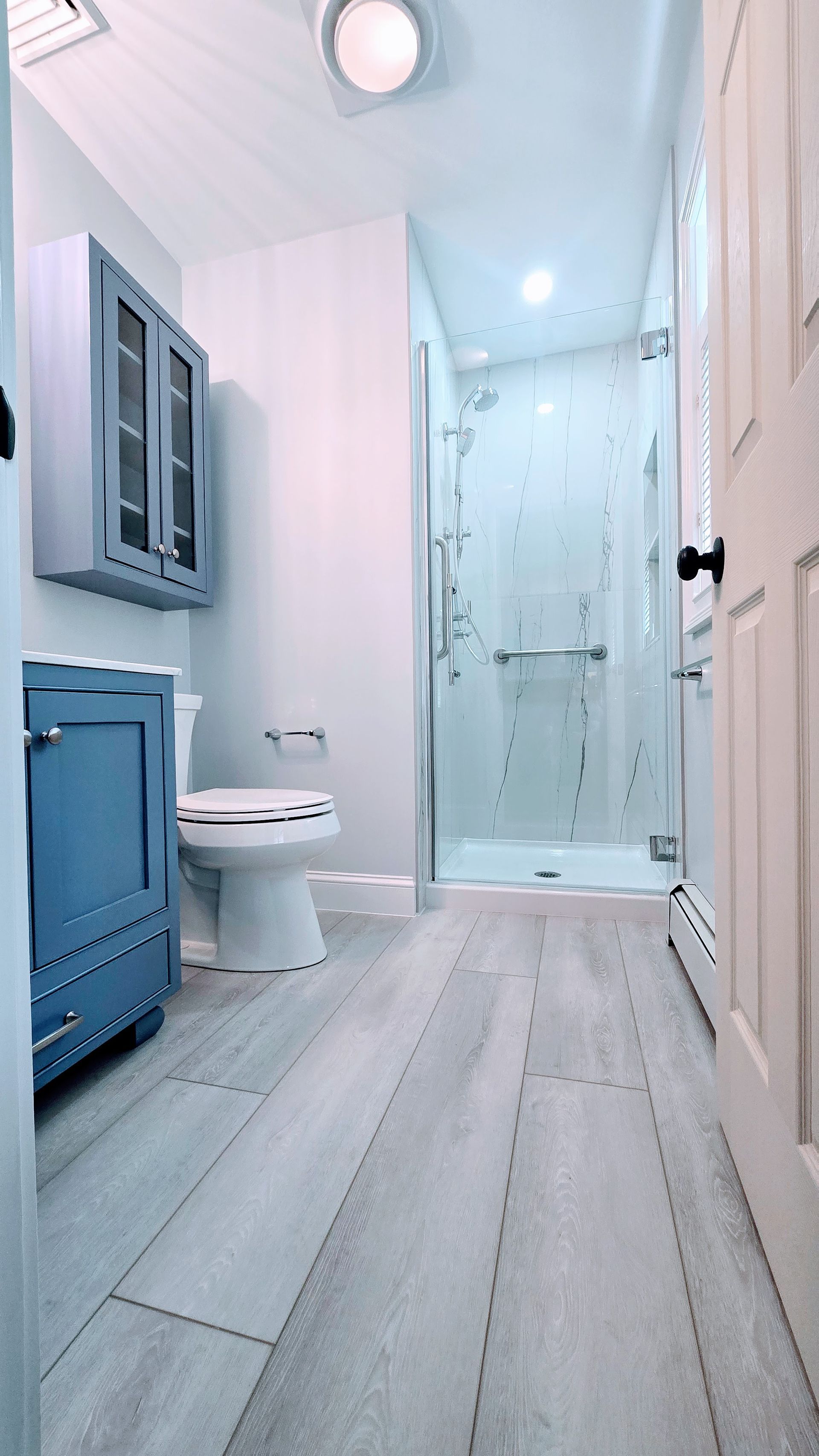 Blue and white bathroom in Cromwell, CT with a shower, toilet, and vanity. Light wood-look flooring.