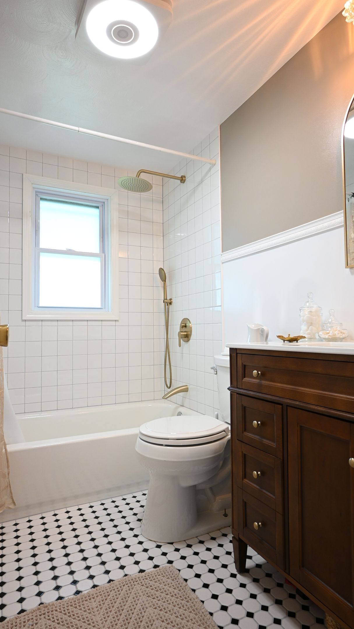 Bright white bathroom with tiled floor, tub-shower, pedestal toilet, window, and dark wood vanity.