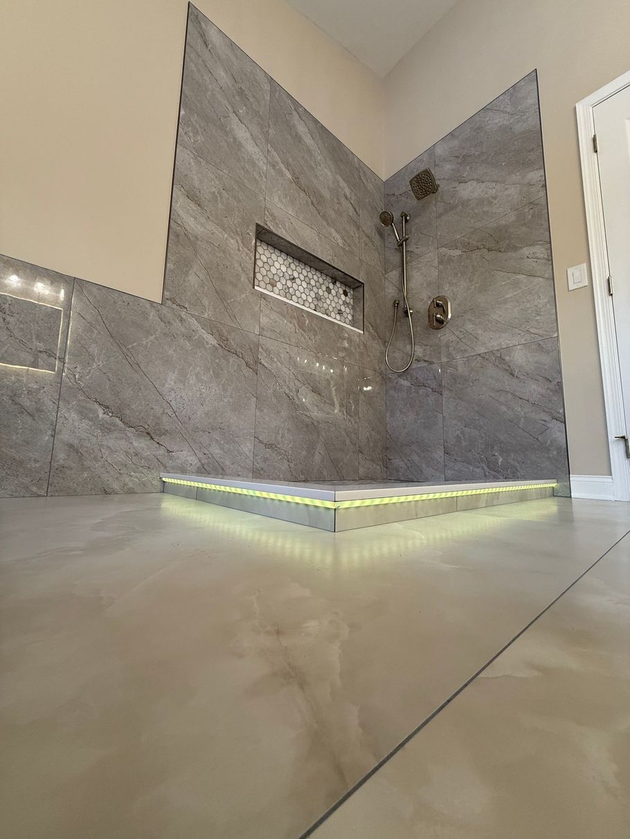 Modern walk-in shower in Glastonbury, CT with gray tiled walls, recessed shelf, and illuminated base; beige floor and walls.