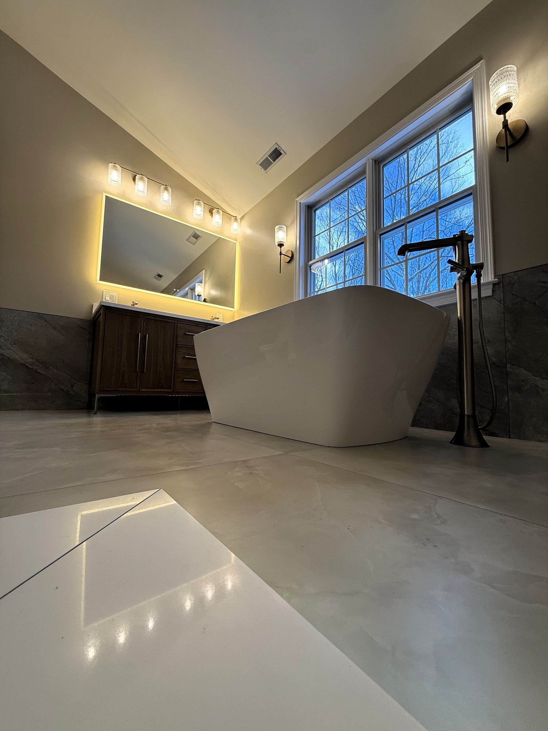 A bathroom with a tub , sink , mirror and two windows.