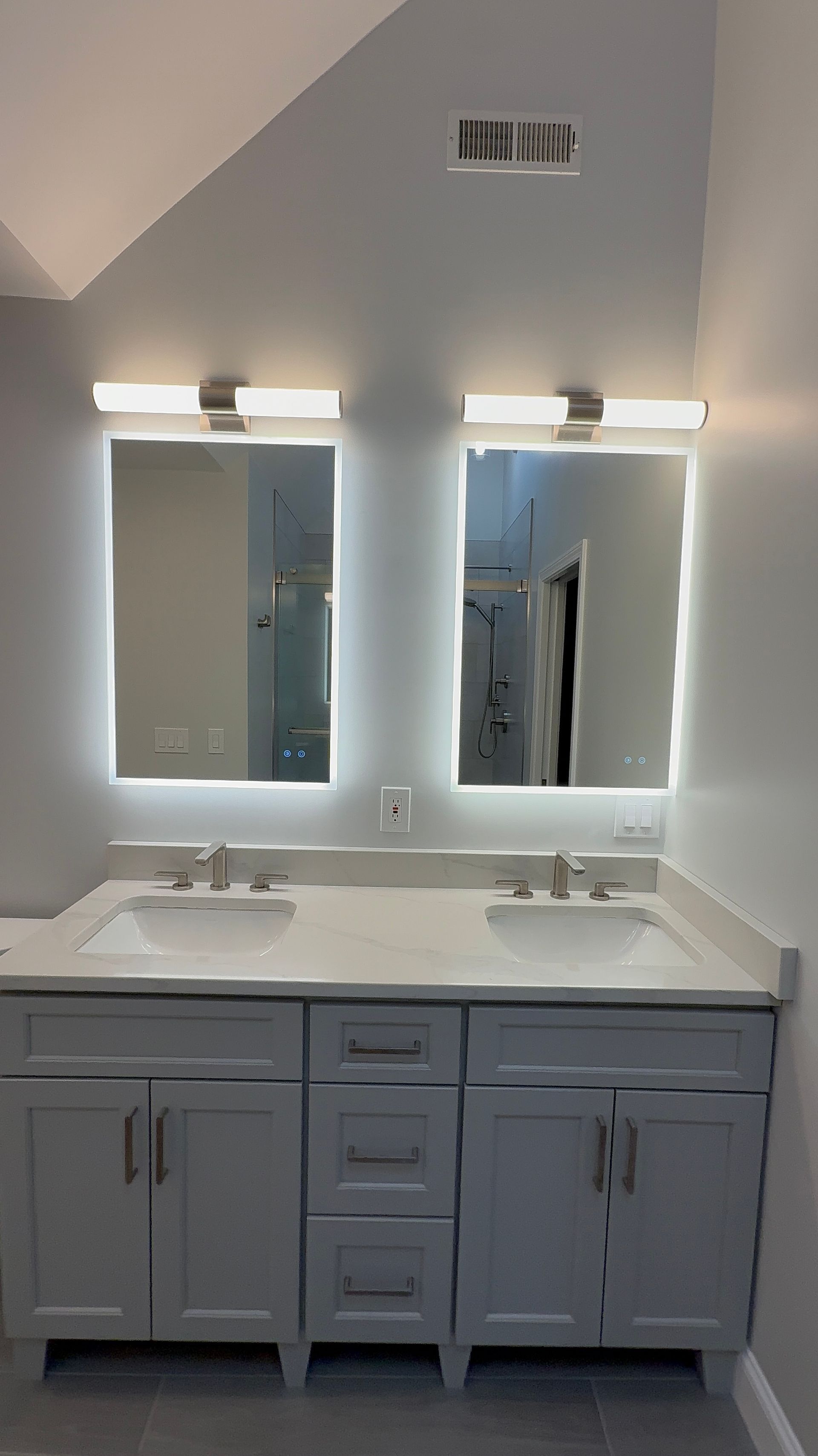 A bathroom with two sinks and two LED mirrors.