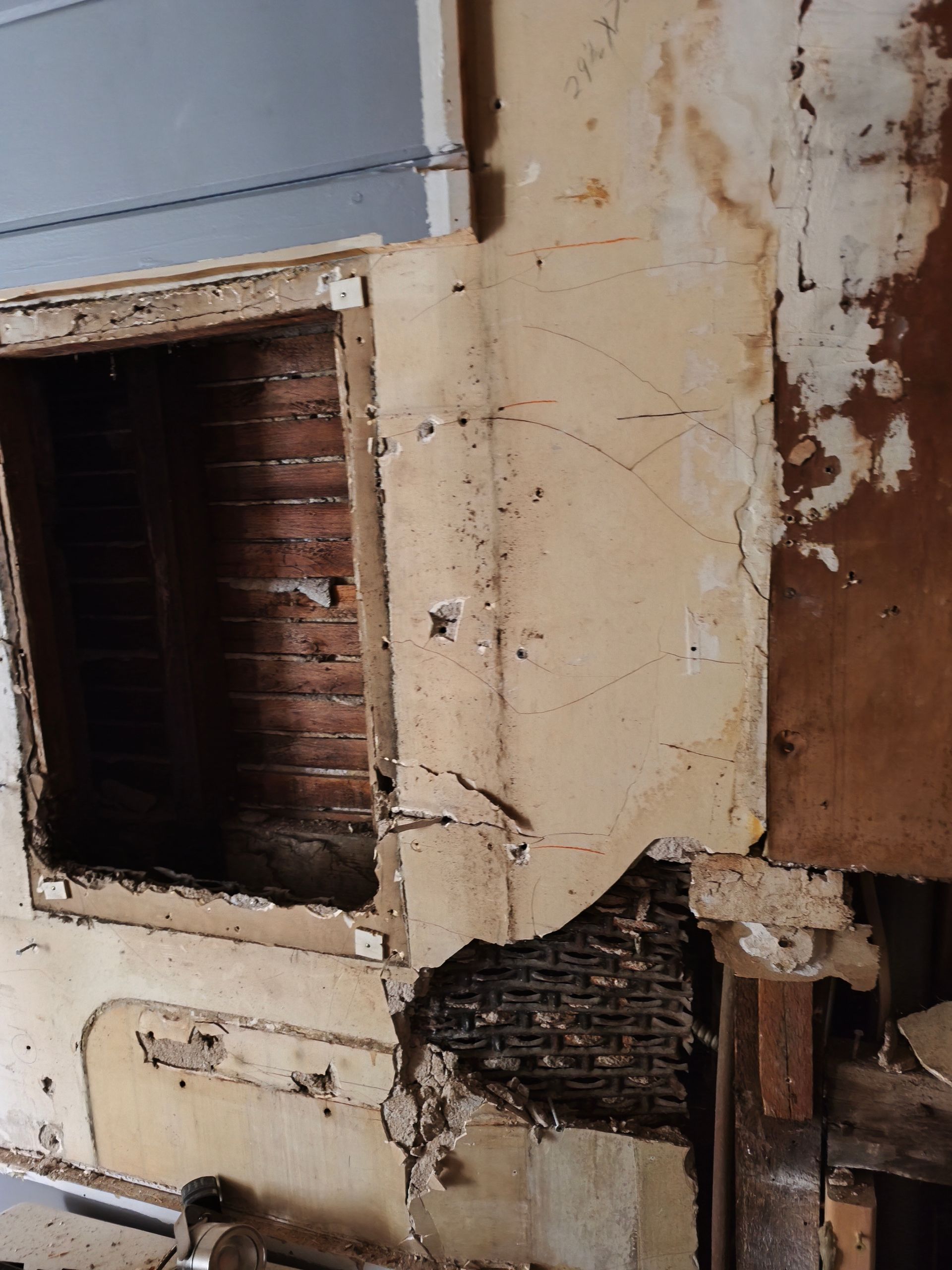 Bathroom remodel in progress: Interior wall with damaged plaster, revealing brick and framing, near an opening.