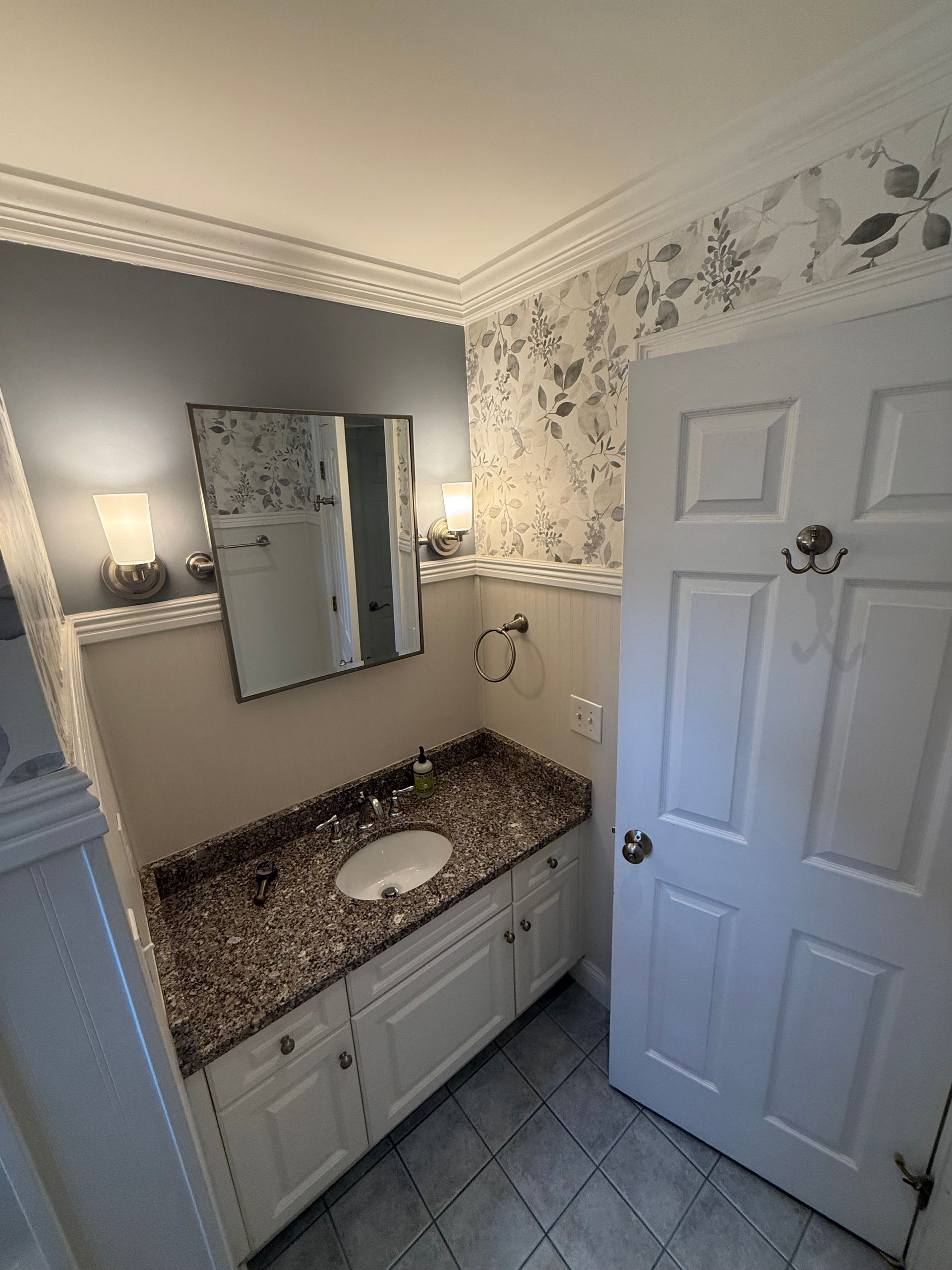 A bathroom with a sink , mirror , cabinets and a door.