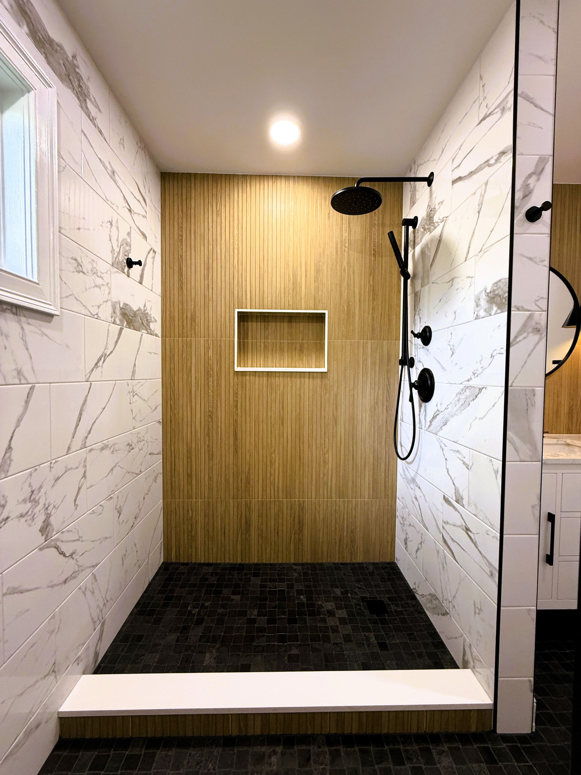 Shower with white marble-look tiles and a black tile niche. Chrome fixtures and a white seat.