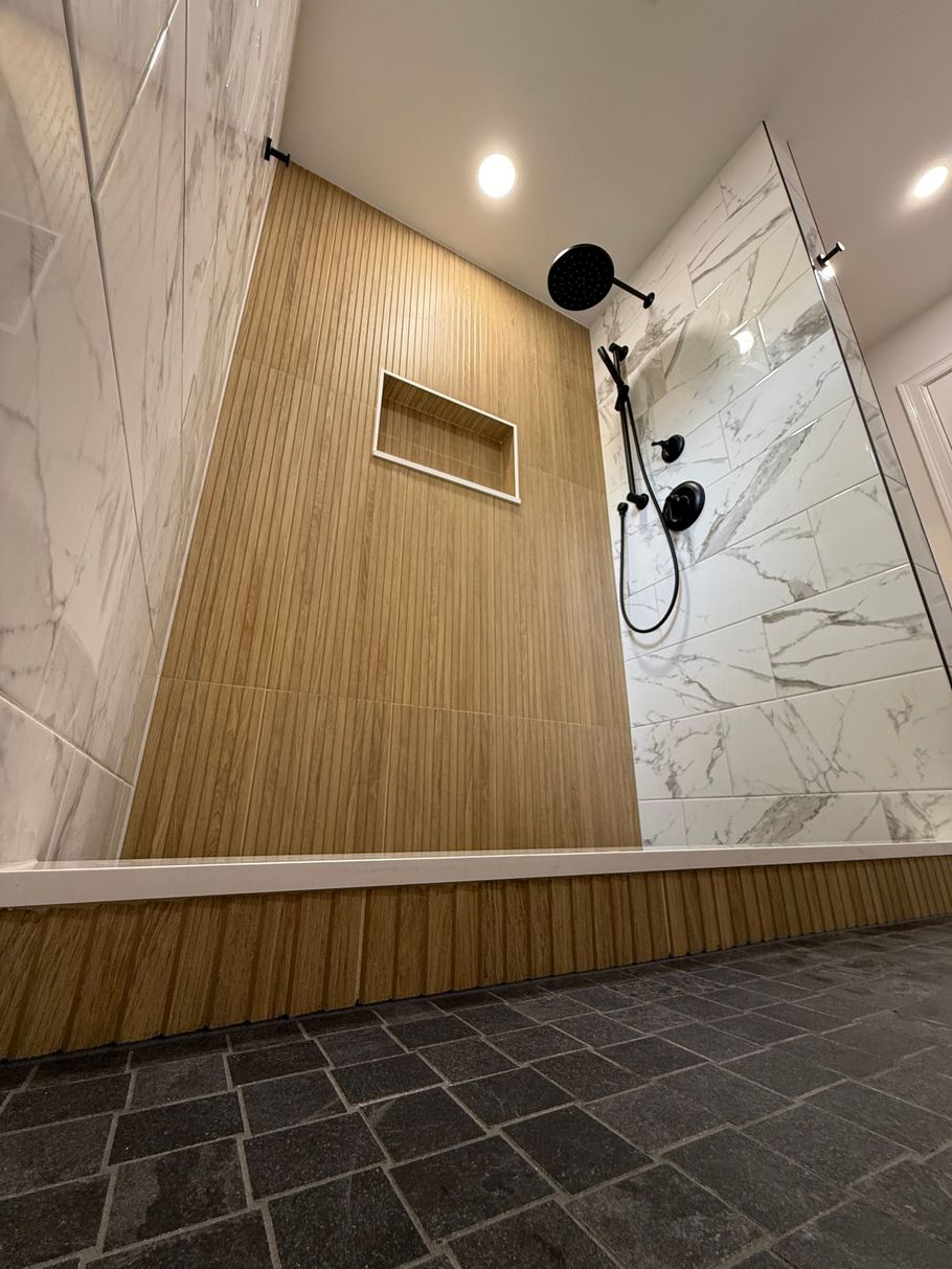 A bathroom with a walk in shower with a wooden wall and marble tiles.